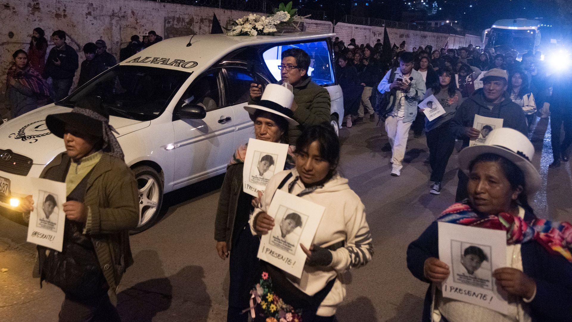 protesters dressed in white march down a street while holding pictures of a person killed by Peruvian security forces