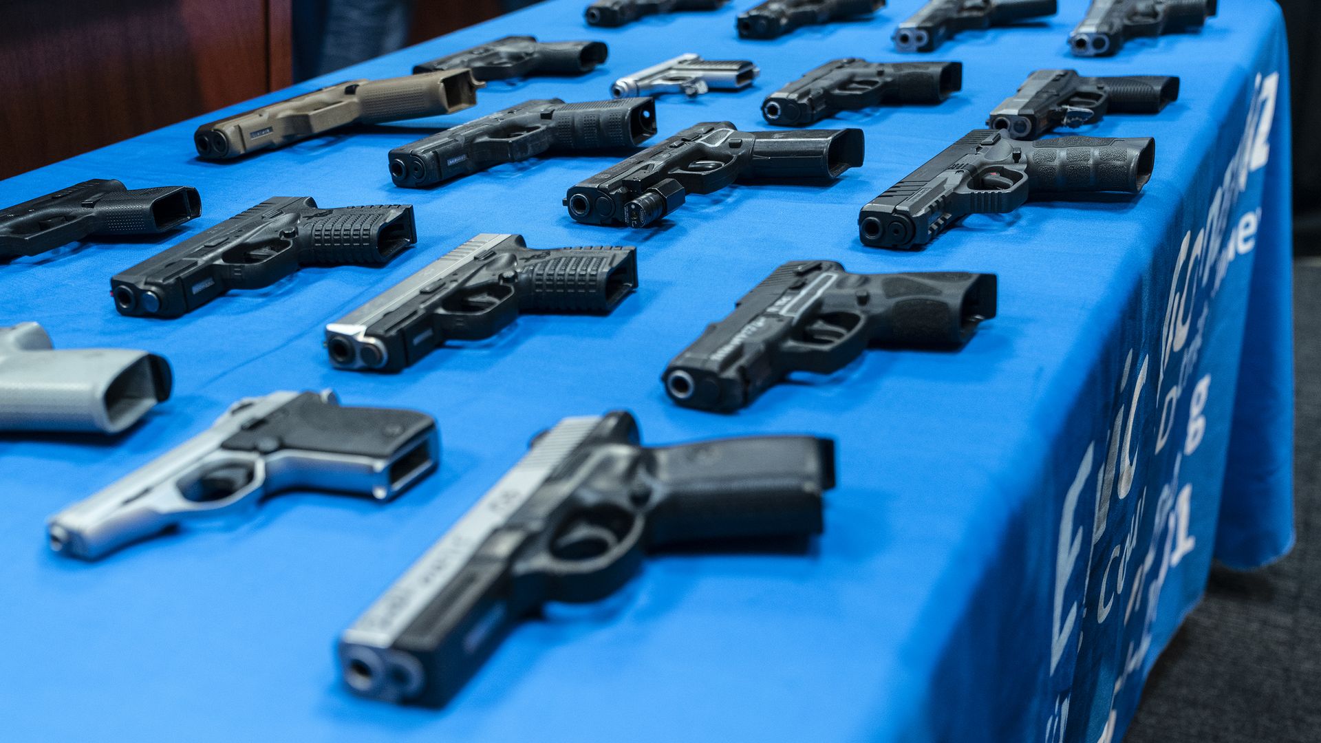Photo of guns laid out in four rows on a blue tablecloth