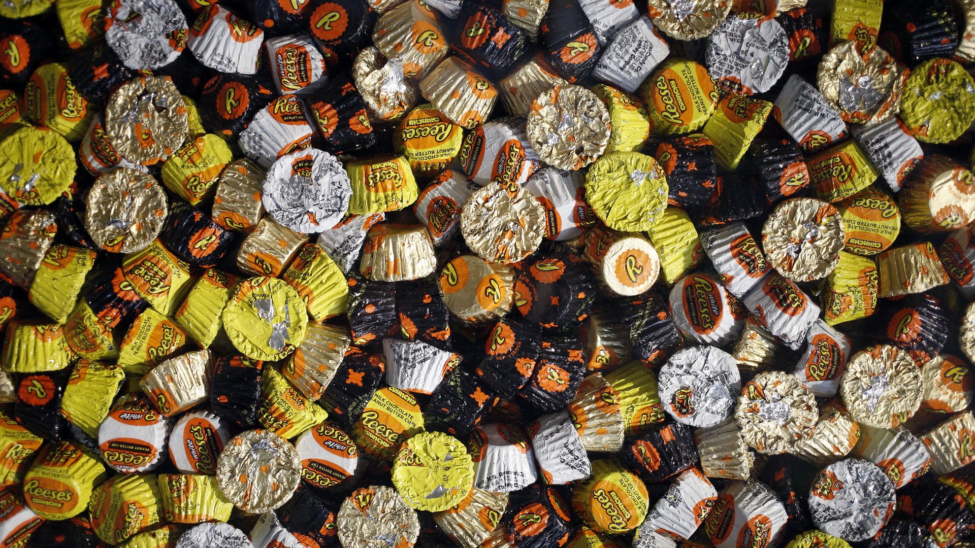 A close-up photo of dozens of Reese's peanut butter cups in white, gold, black and yellow wrappers.