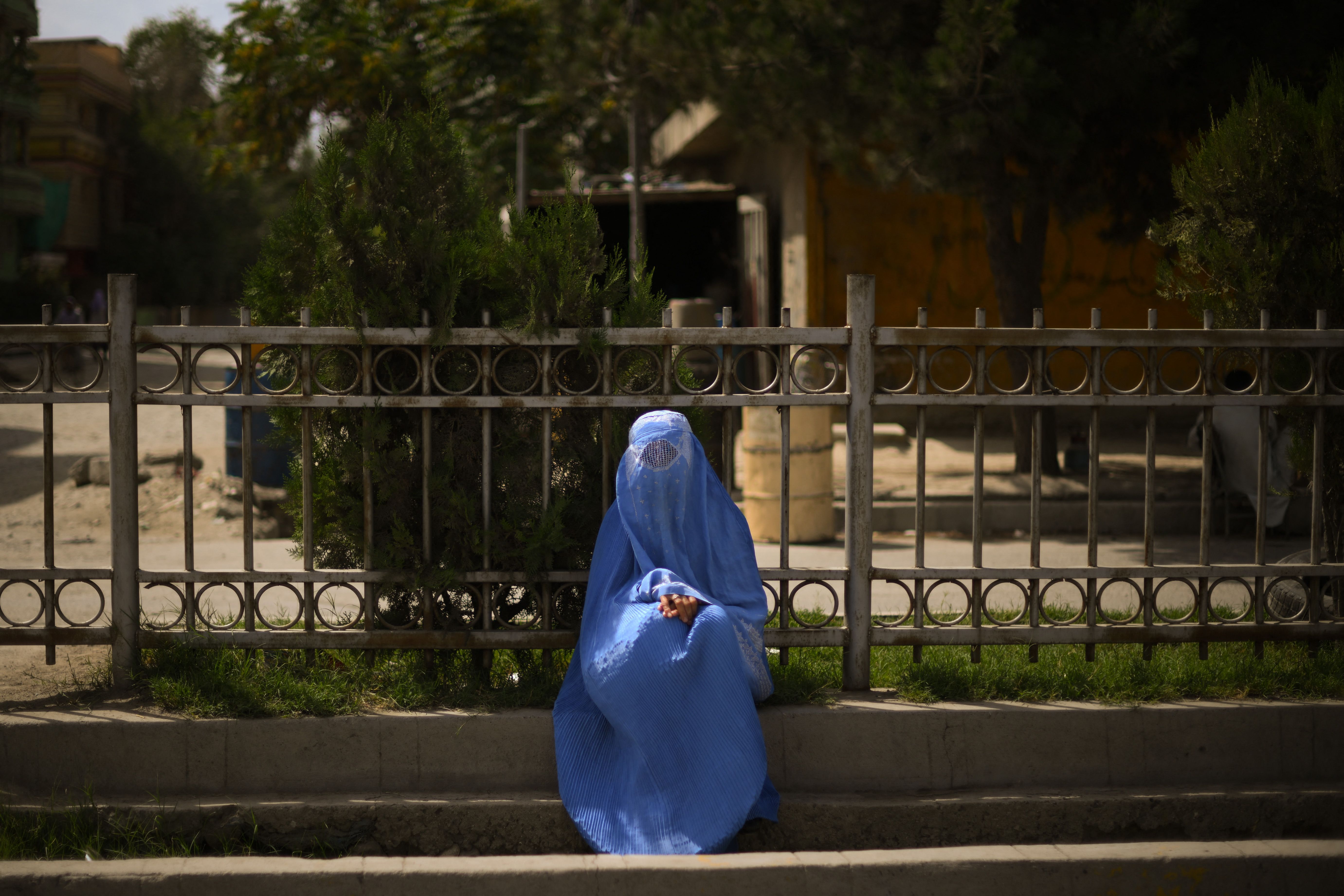 A woman wearing a burqa, seated on the side of the road. 