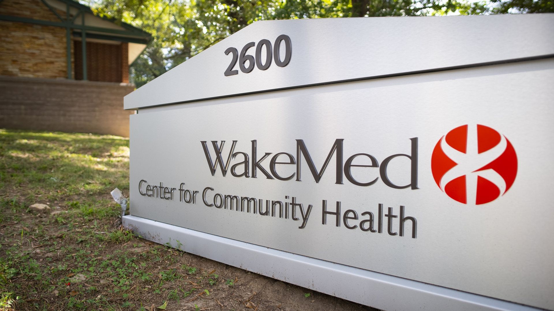 Outdoor white sign showing the number 2600 at the top, with WakeMed and Center for Community Health text and a red circular logo on the right, brick building and trees in background.