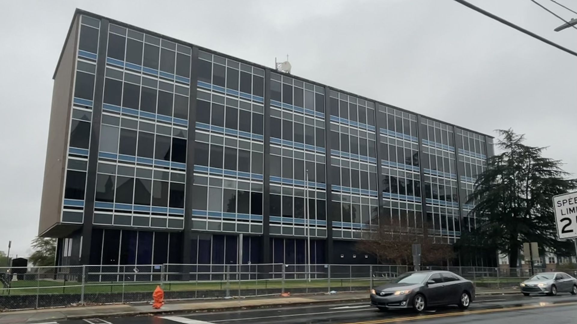 A mid-century modern building stands in the rain with traffic going before it. 