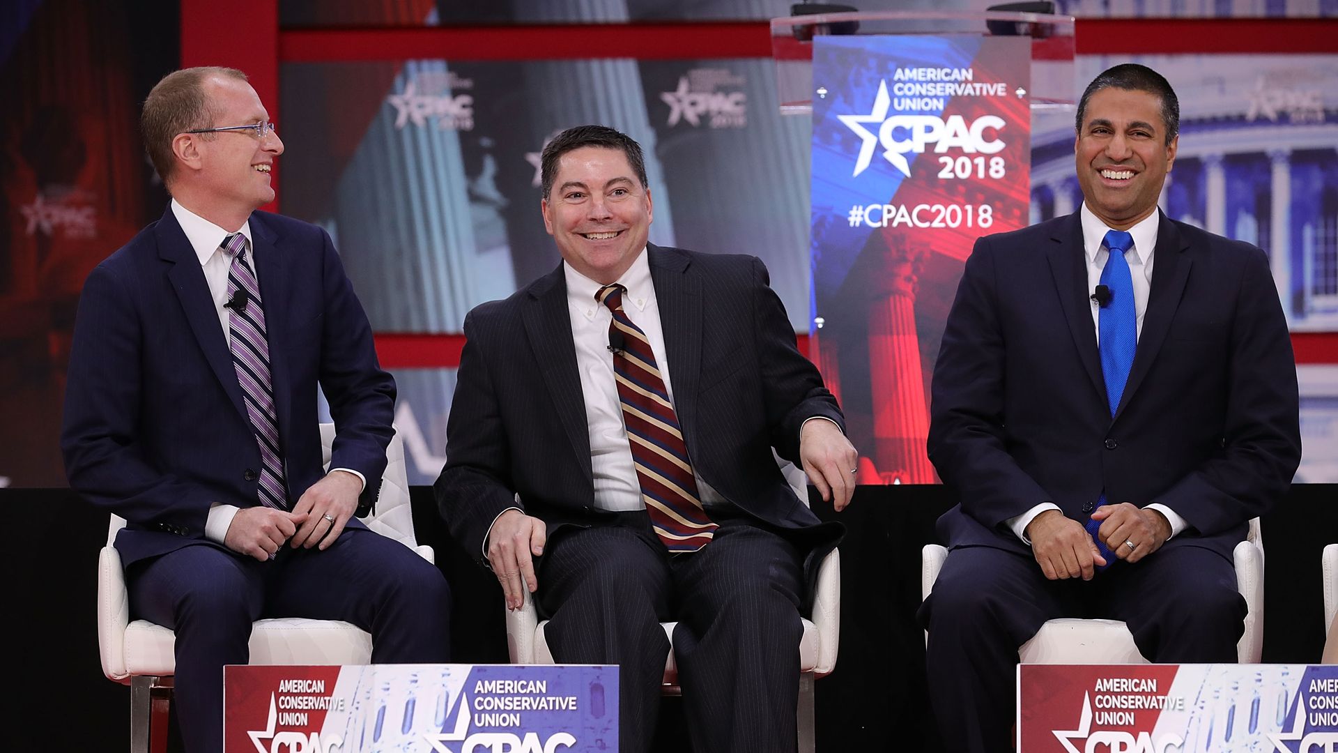 Three FCC commissioners laughing on a stage