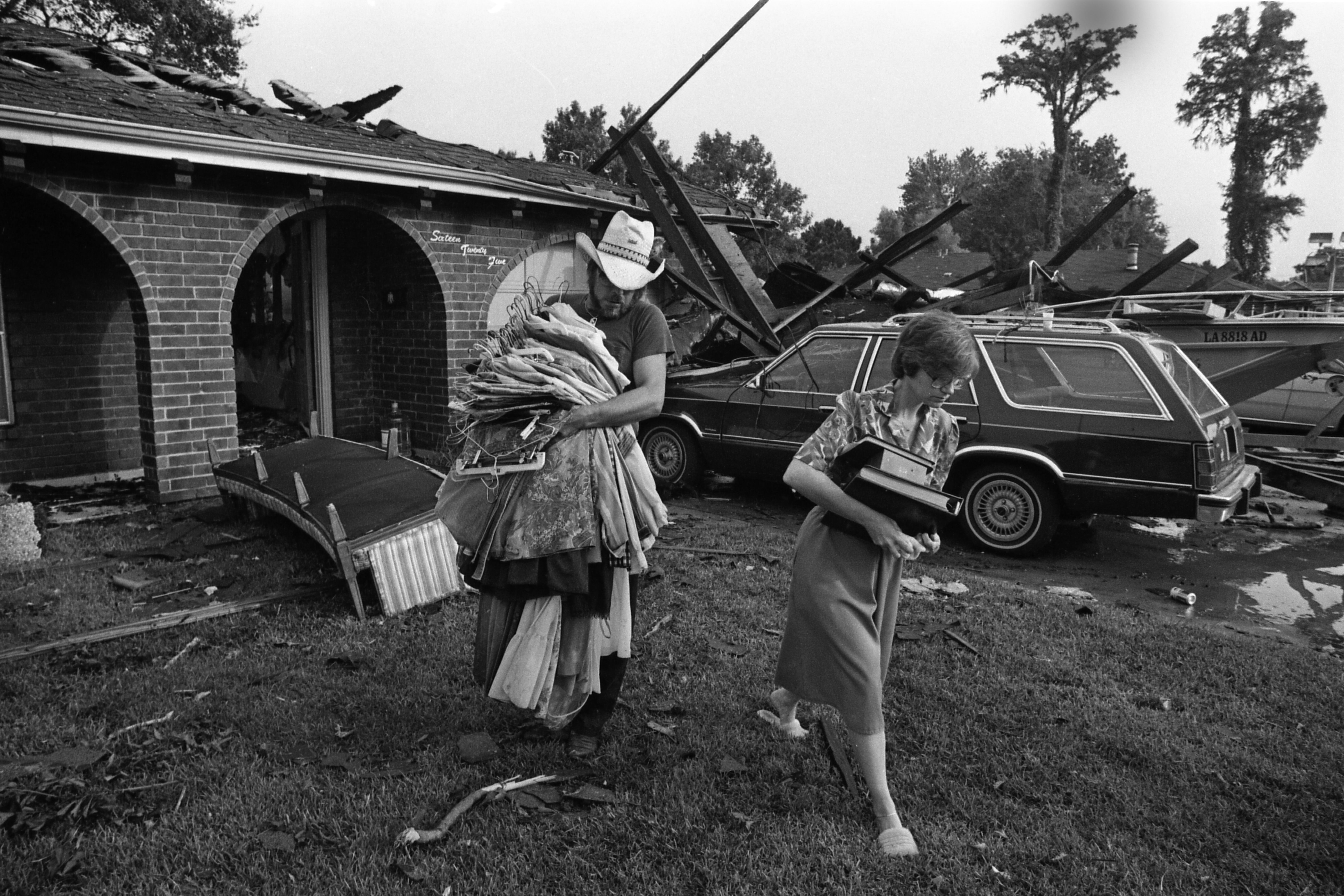 Photo shows two people taking clothes out of a destroyed home.