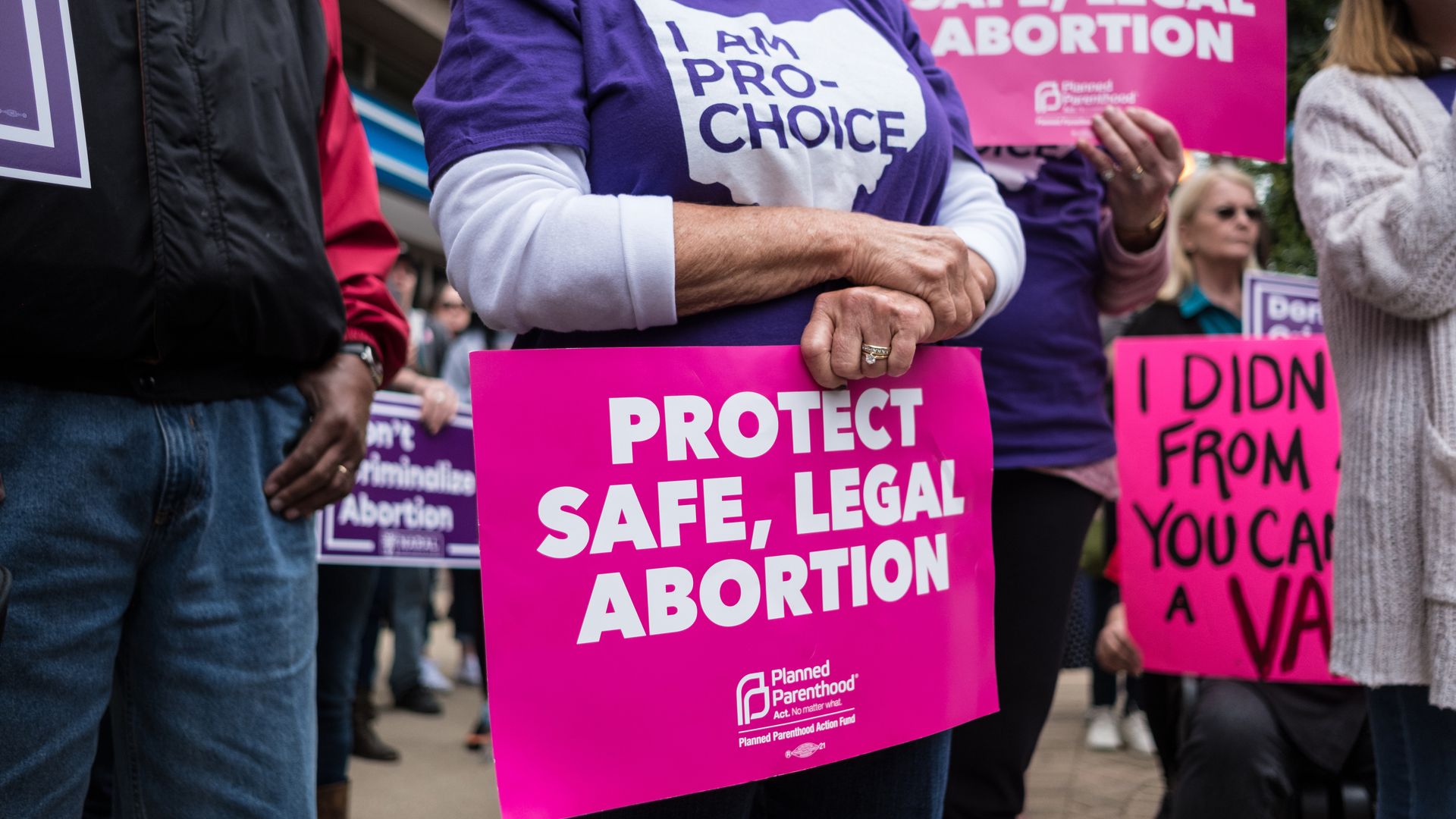 A woman holds a "protect safe, legal abortion" sign in her hands.