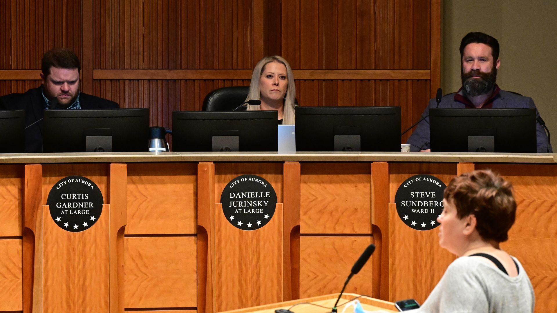 Three people sit behind a raise podium structure behind computer screens. 