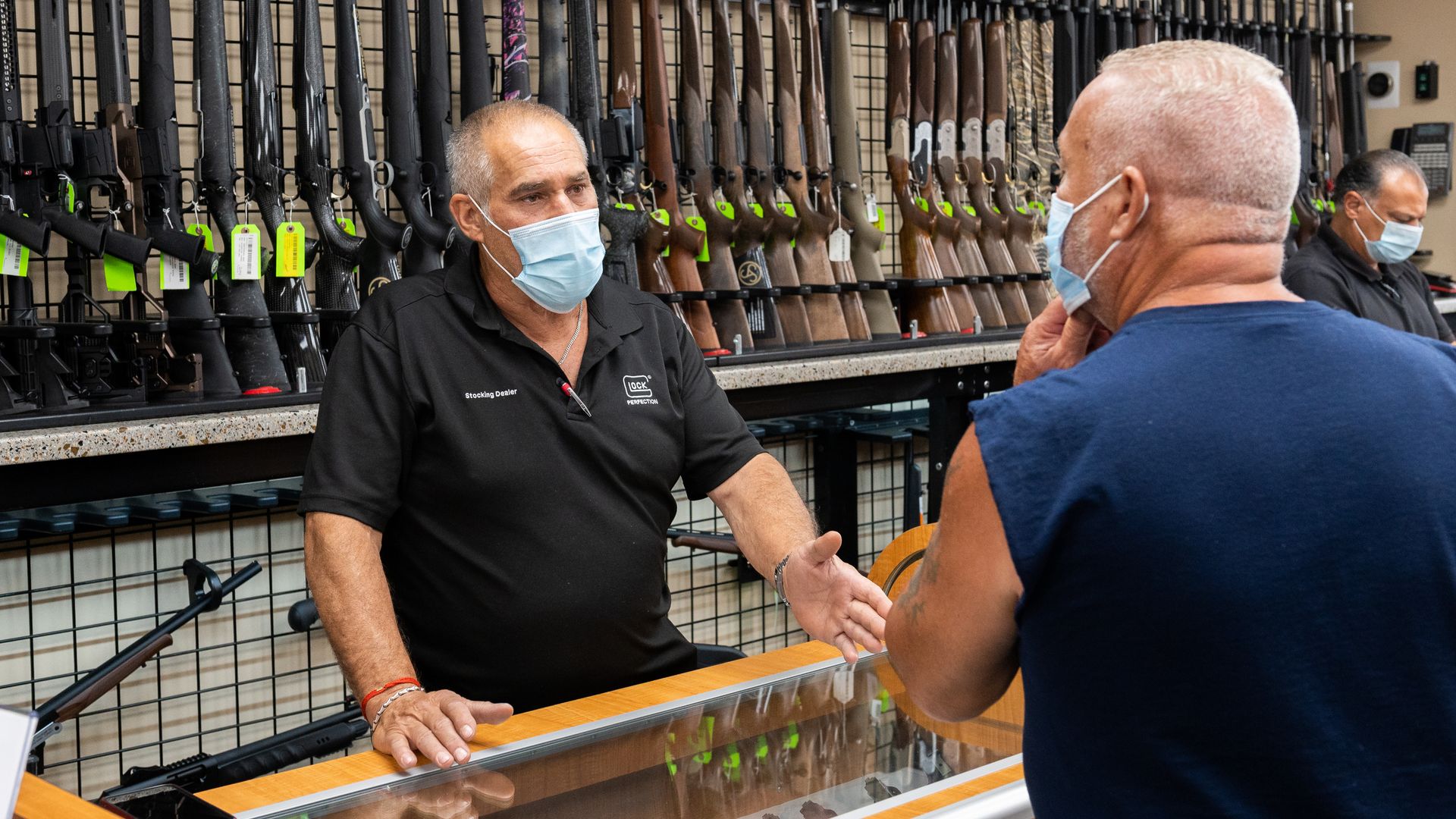 A gun shop employee speaks to a customer while wearing a face mask
