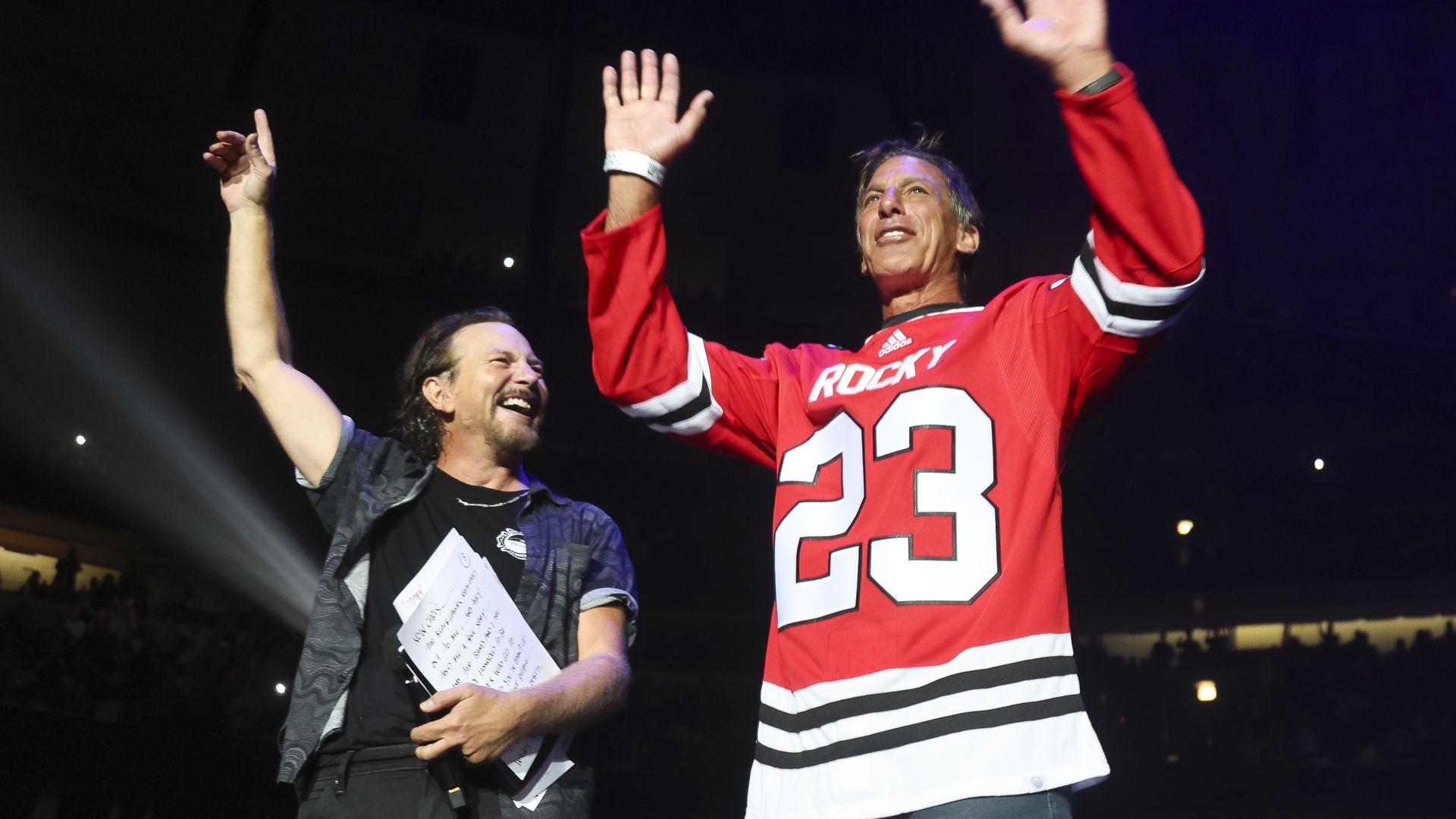 Photo of two people on stage with their hands up 