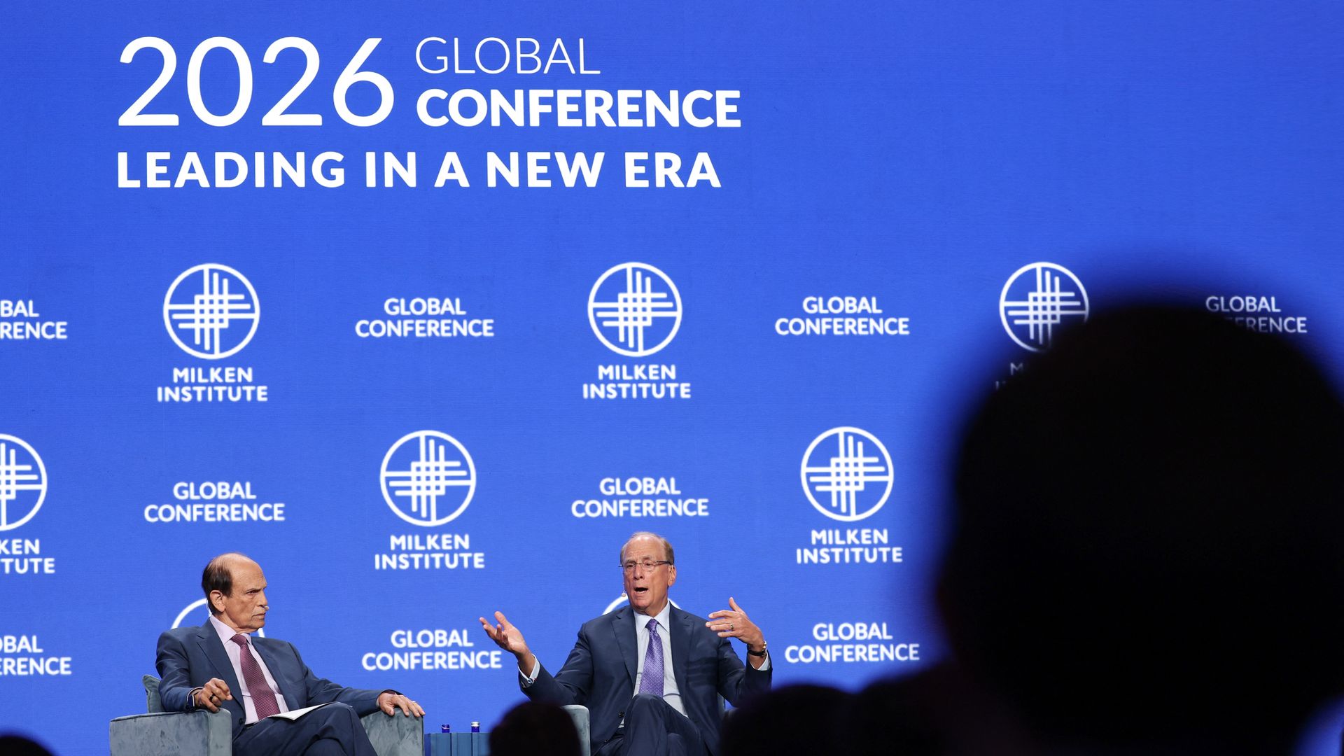 Michael Milken and Larry Fink, seated in chairs on a stage at the Milken conference. 