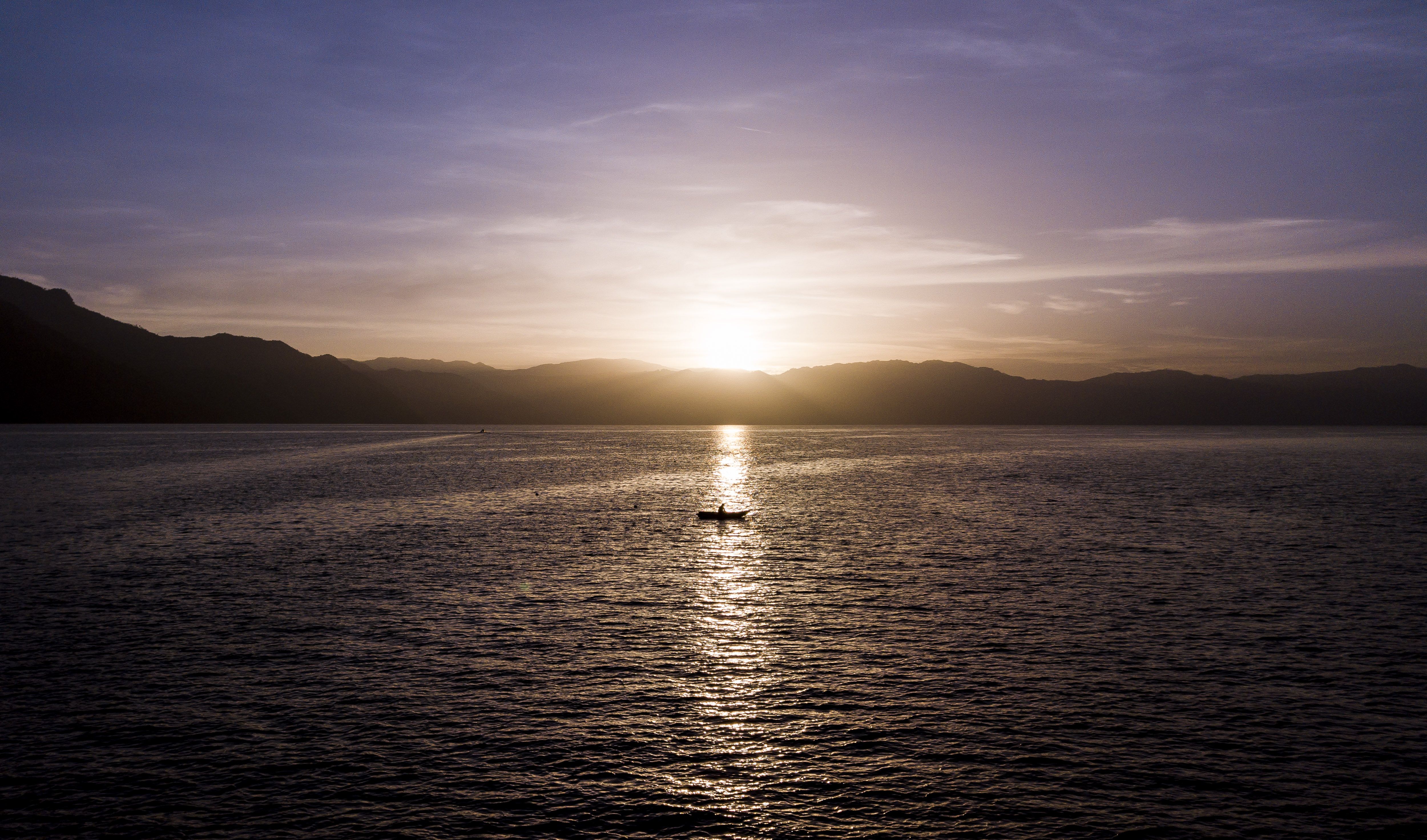 A man fishes under the warm light of sunrise at Lake Atitlán in August 2018, in Sololá Department, Guatemala.
