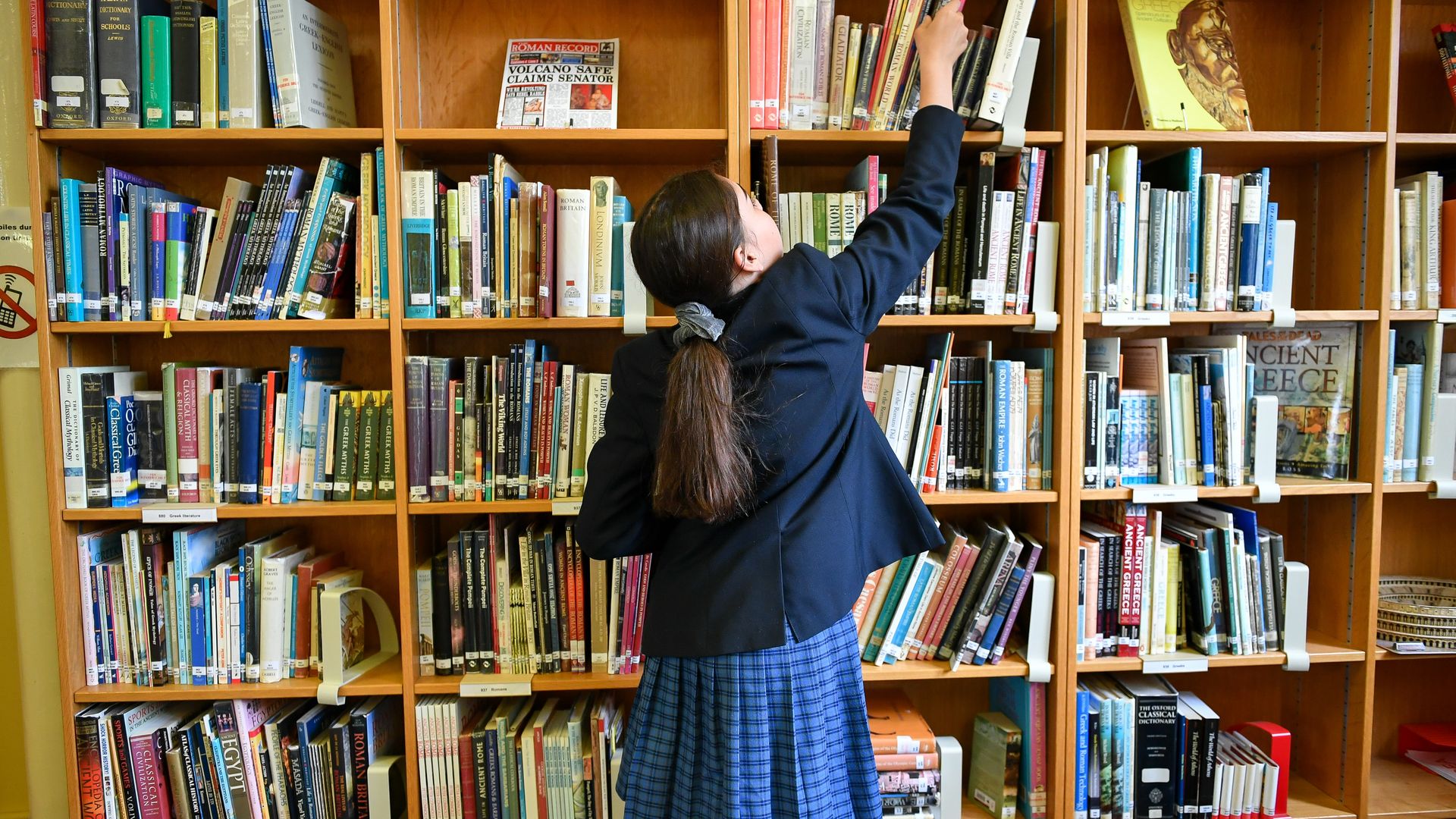Girl reaching for a library book.