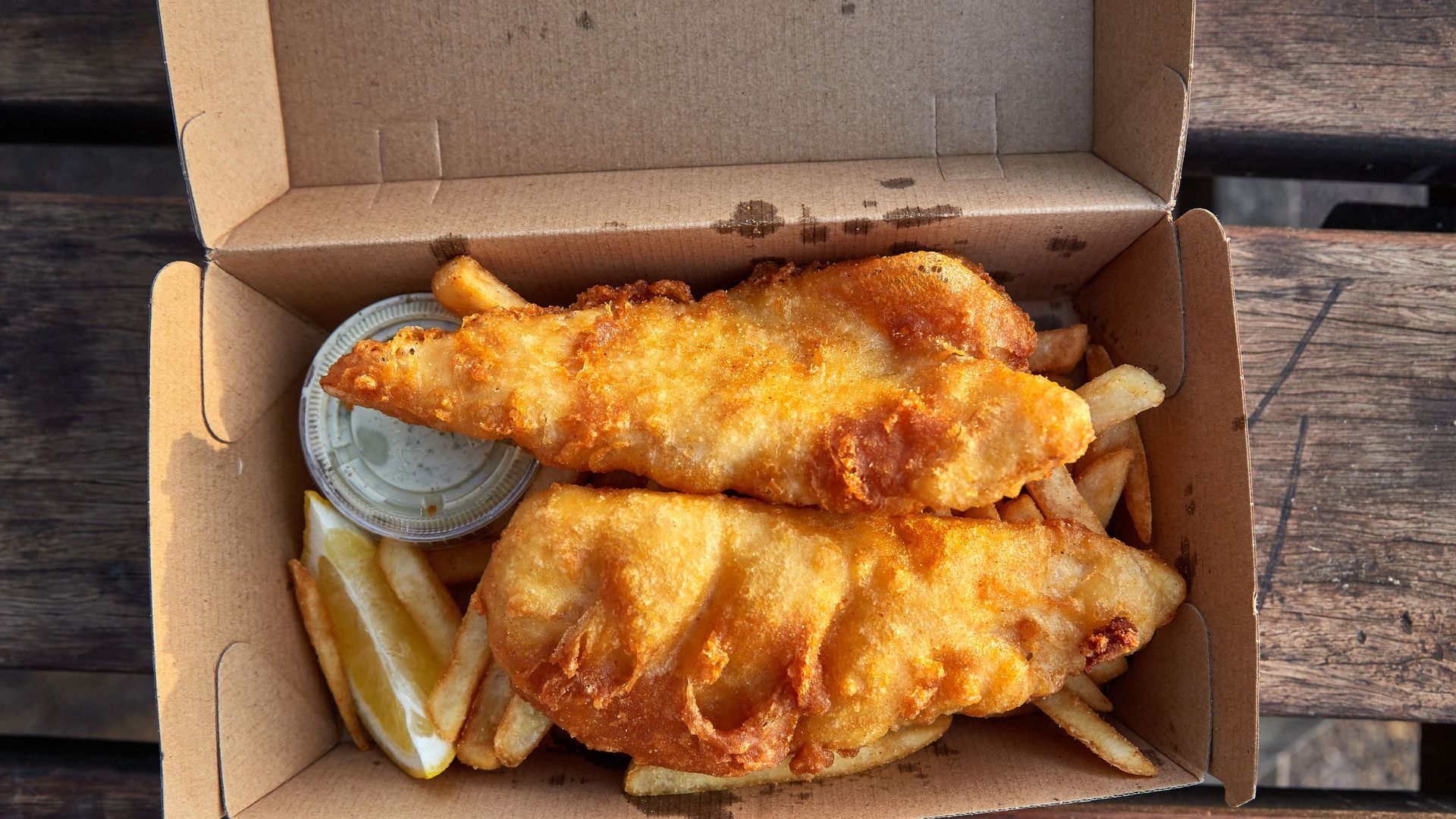 Two pieces of fish on top of fries in a cardboard box