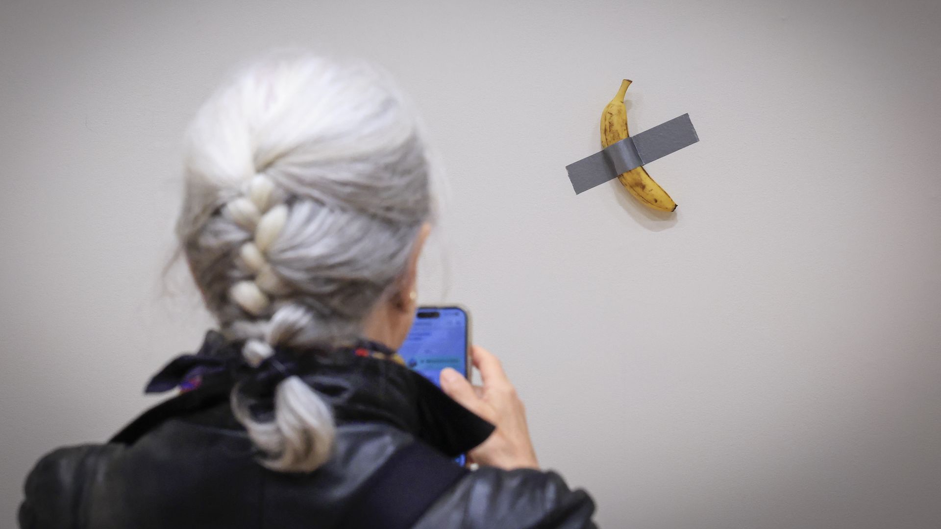 A journalist takes a photo of artist Maurizio Cattalan's artwork "Comedian," a banana duct-taped to a wall.