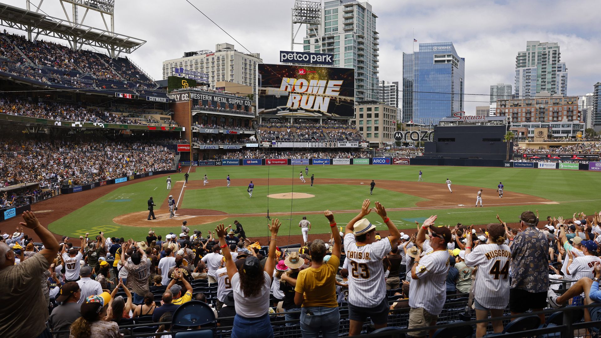 A view of the field at Petco Park as fans raise cheer and high five in the stands of a San Diego Padres game after a home run.