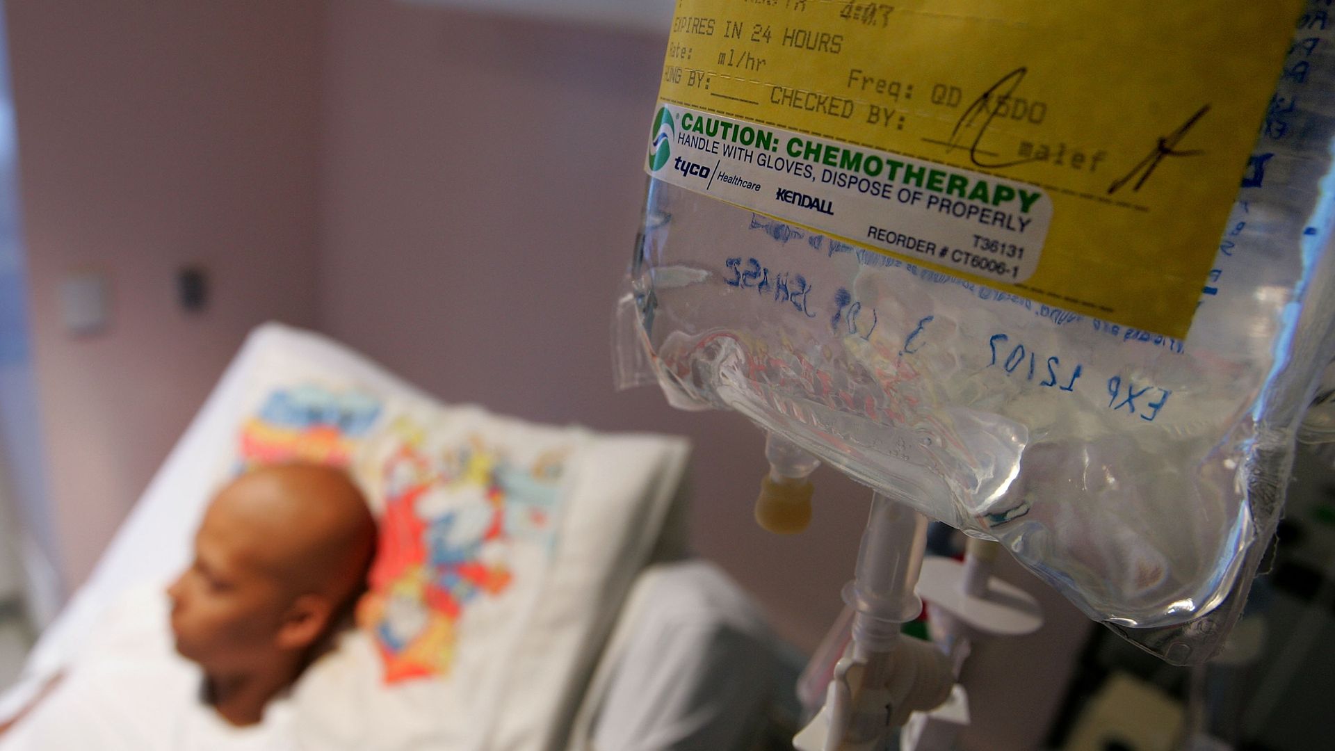 IV drip seen in foreground while young man lays in hospital bed.
