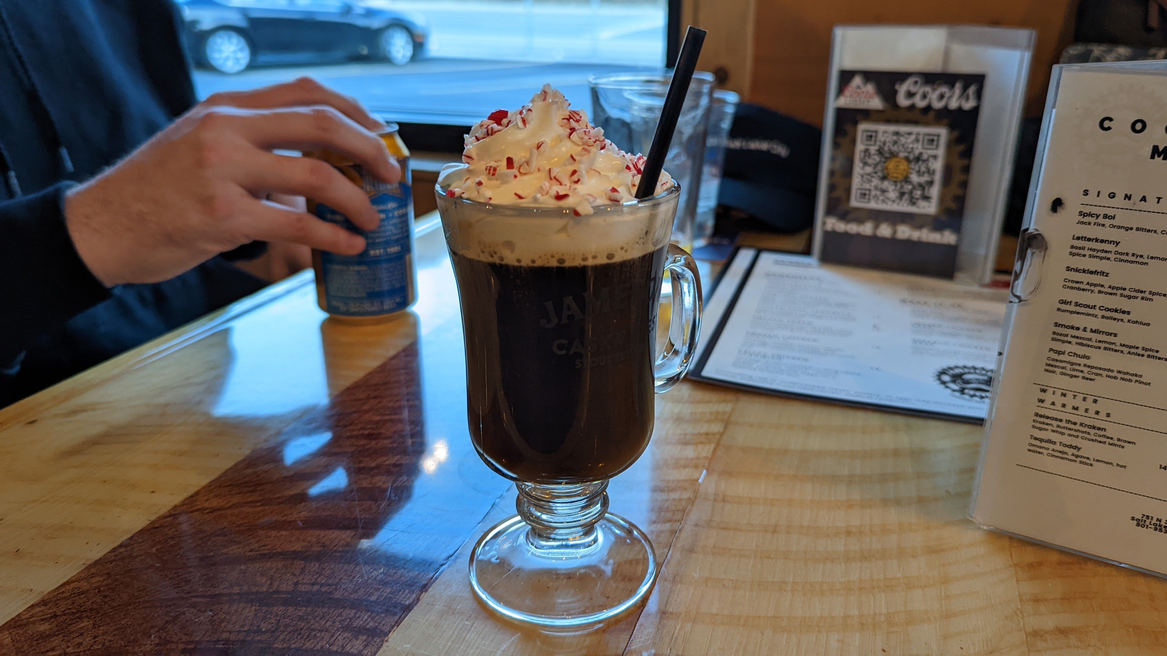 A coffee cocktail with whipped cream is on a table next to a man drinking beer.
