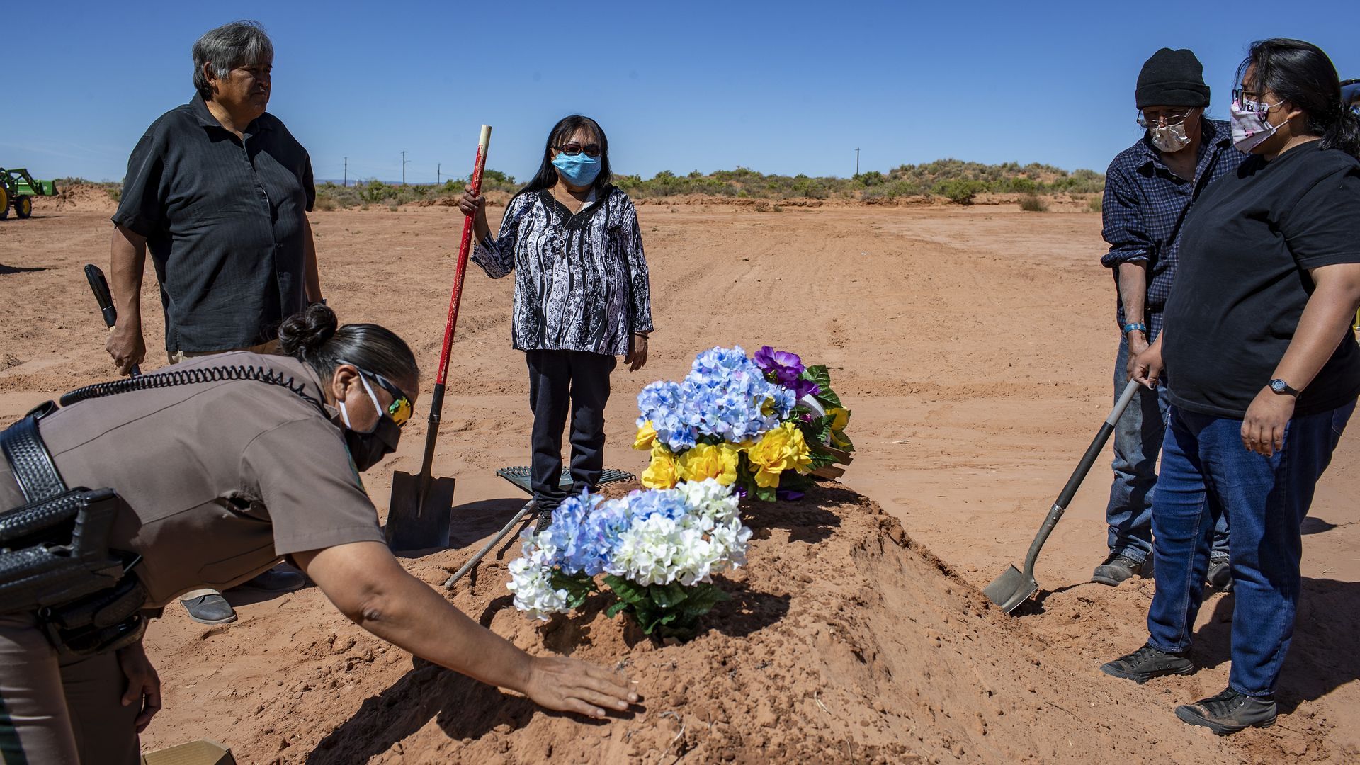 Carlita Bergen holds a shovel as Navajo Nation police officer Carolyn Tallsalt smooths dirt over COVID-19 victim Arnold Billy's grave in Tuba City, Arizona.