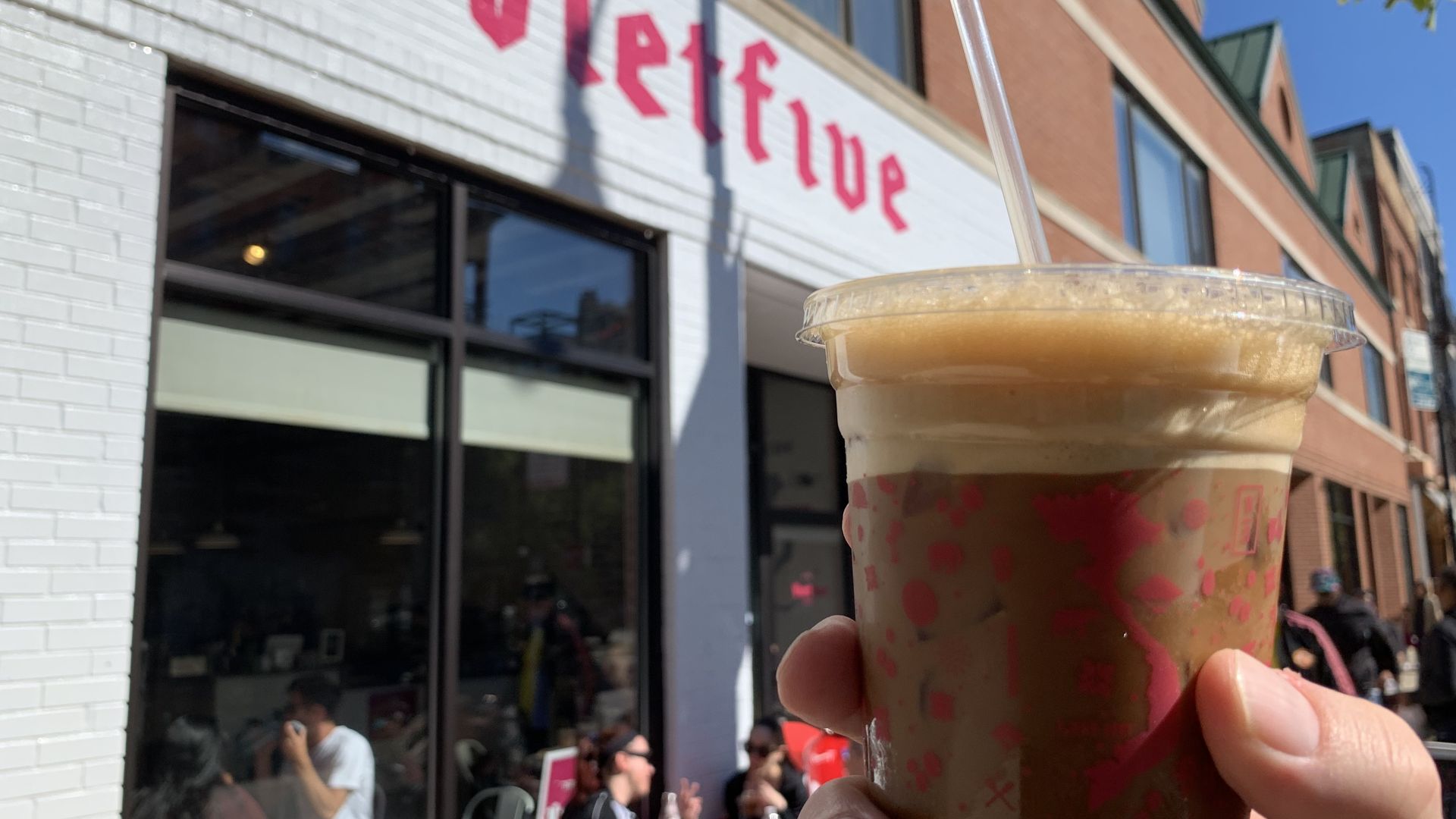 Photo of a man holding a coffee drink in front of a store.