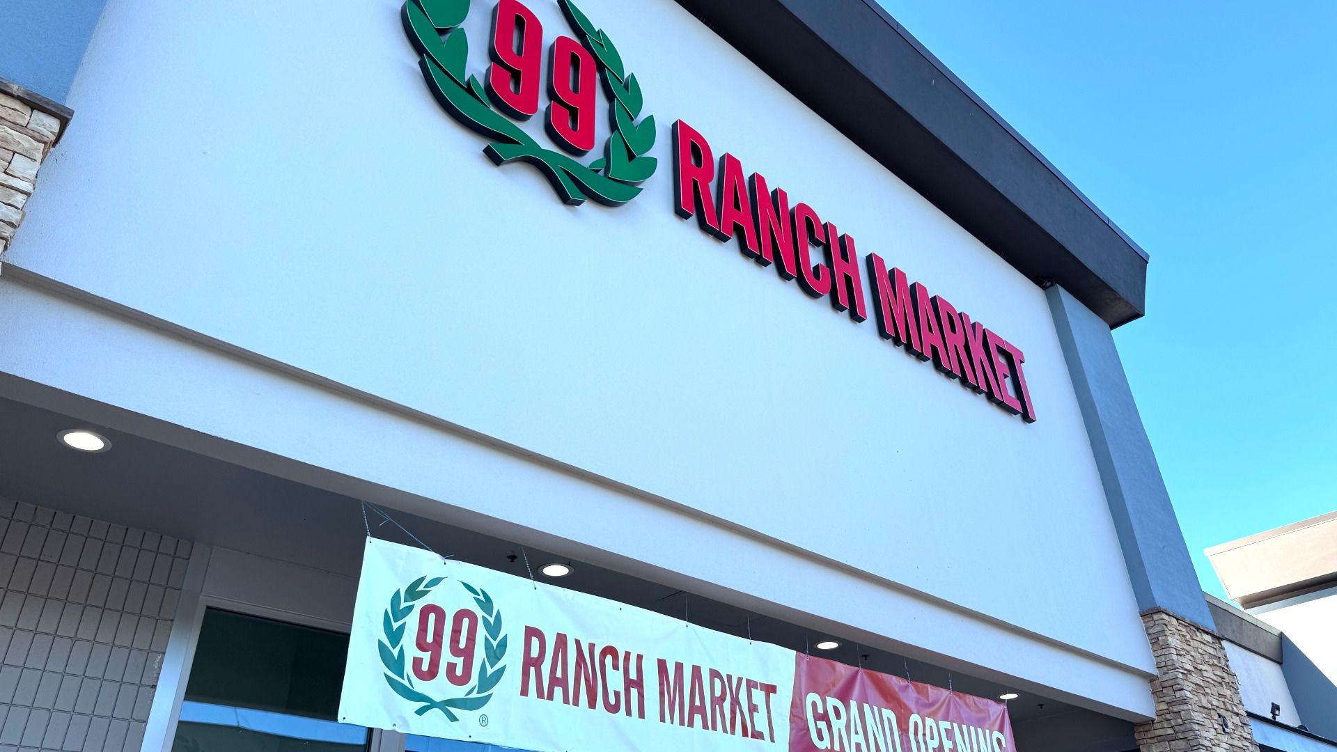 Building exterior with clear sky, featuring large red lettering "99 Ranch Market" and a banner below announcing "99 Ranch Market Grand Opening".