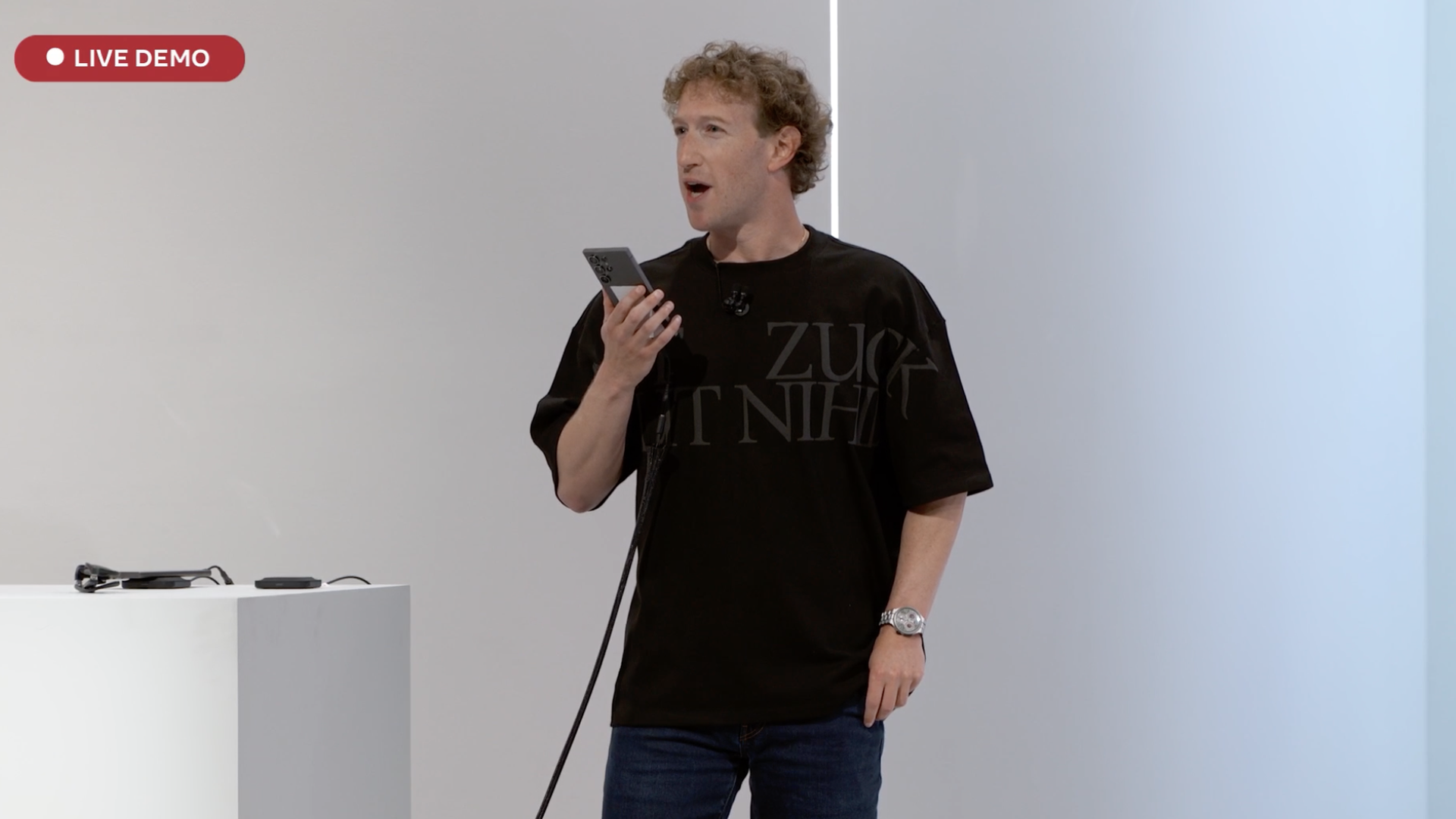 Mark Zuckerberg talking to a cell phone on a stage with the words "LIVE DEMO" in red over the screen.