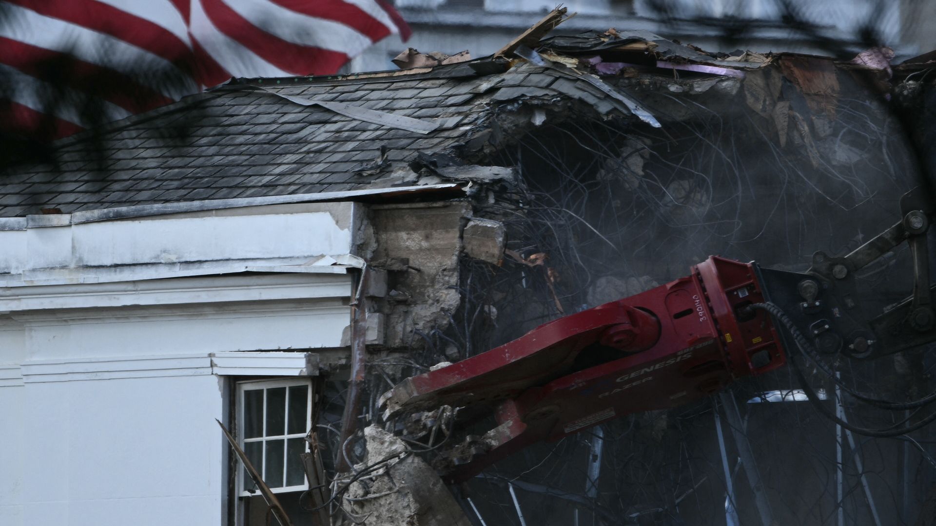 Heavy machinery tears down a section of the East Wing of the White House with an American flag in the background. 
