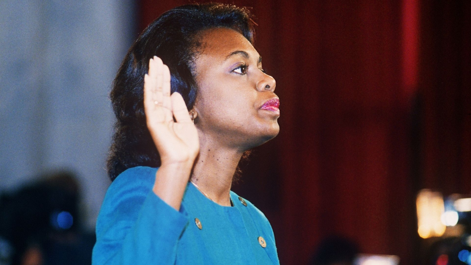 An old photo of Anita Hill testifying in front of the Senate in a bright blue suit