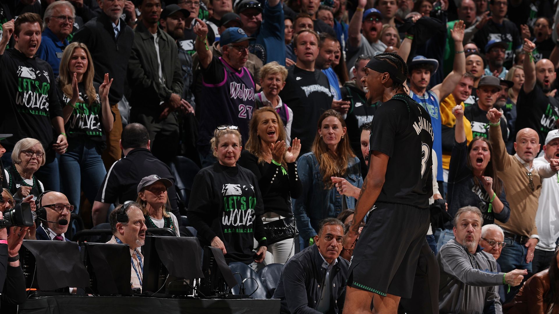Basketball player in a black jersey walks along the court as a packed crowd cheers with raised hands behind him; ESPN NBA logo visible on the barrier in front.