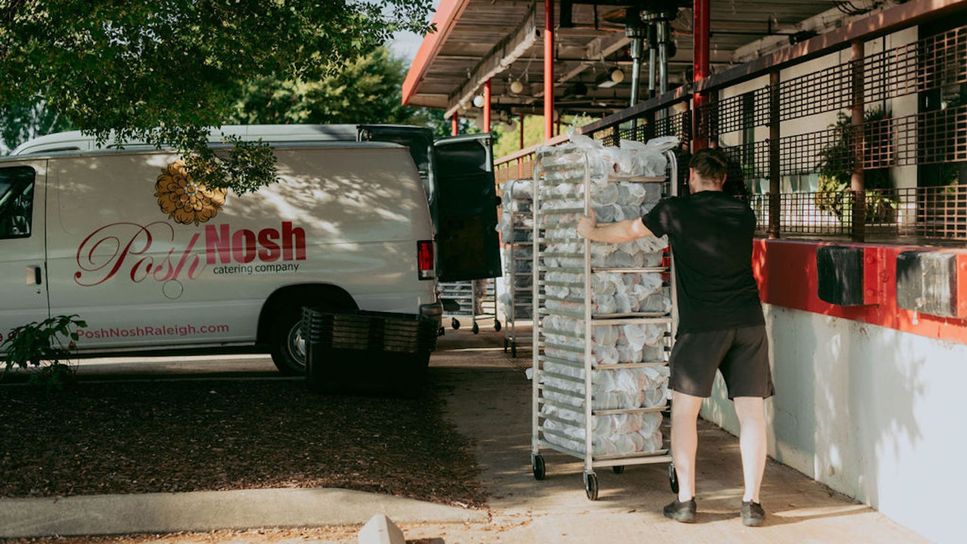A man pushes food in a cart toward a white van.
