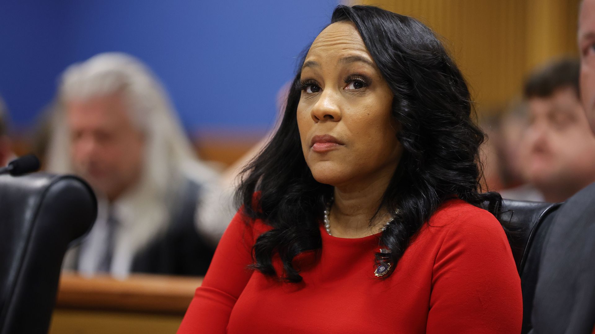 A woman wearing a red dress sits in a courtroom.