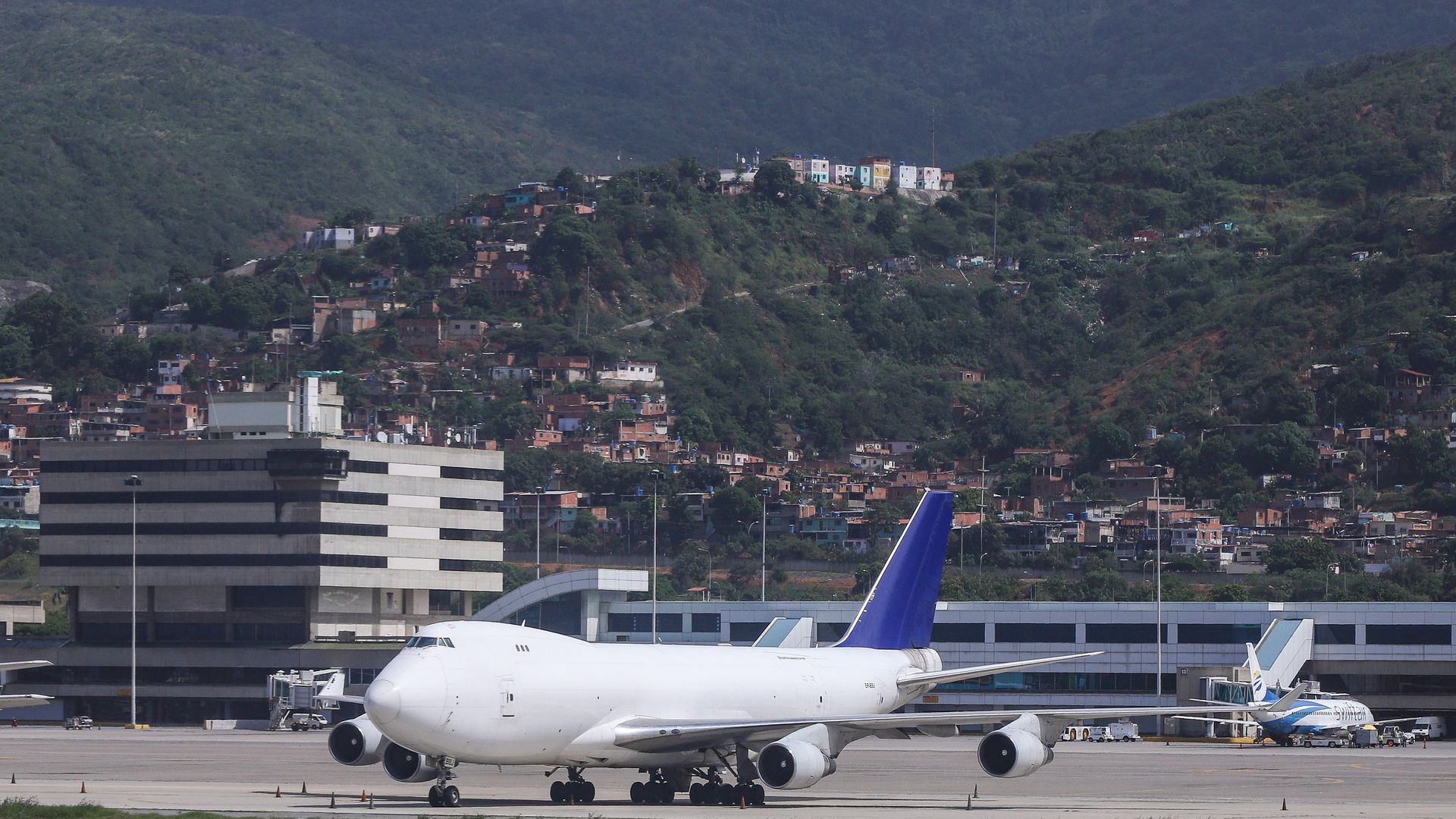 A white Boeing 747 Cargo plane with a blue tail parked in front of the Terminal of the airport. Terminal, ramp and airport overview of Caracas Airport, Simón Bolívar International Airport in Venezuela CCS/SVMI.
