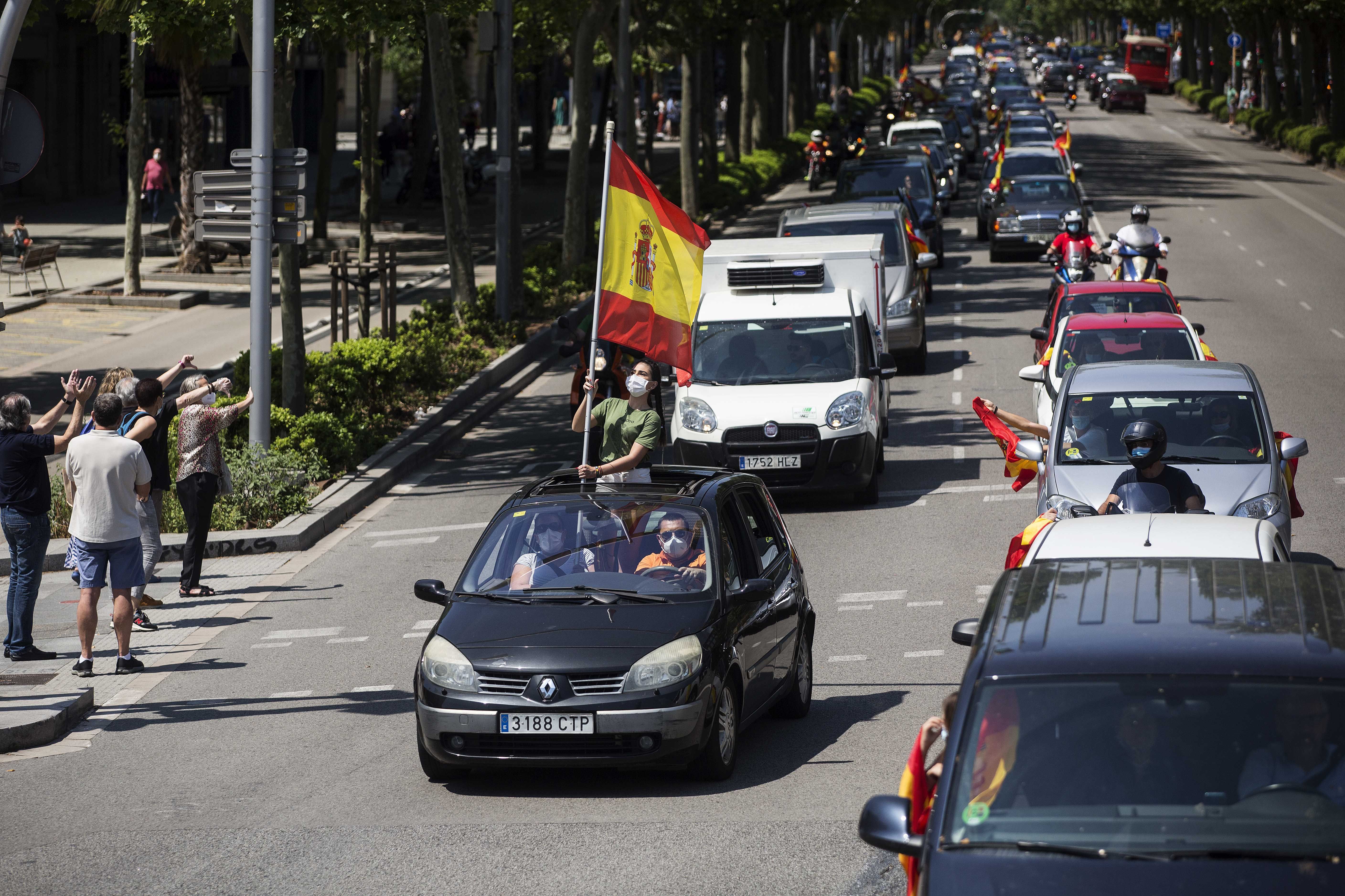 In this image, two lines of cars are on a road and several have people holding flags