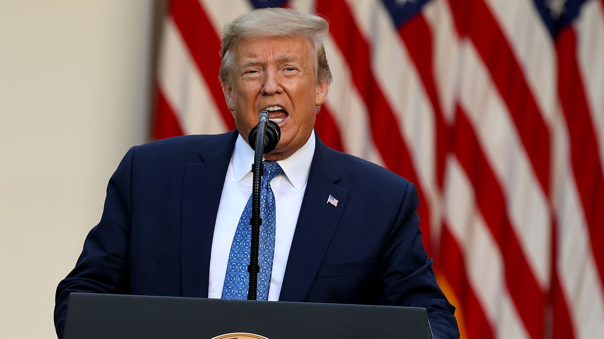 Trump stands behind a podium and American flags