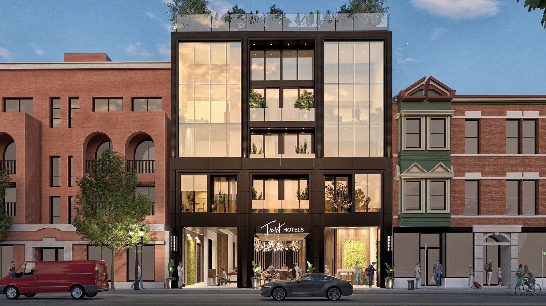 Modern glass-front hotel centered on a city street, between red brick buildings. Large windows show interior plants and people; rooftop greenery, pedestrians, a red van, and a gray car on the street.