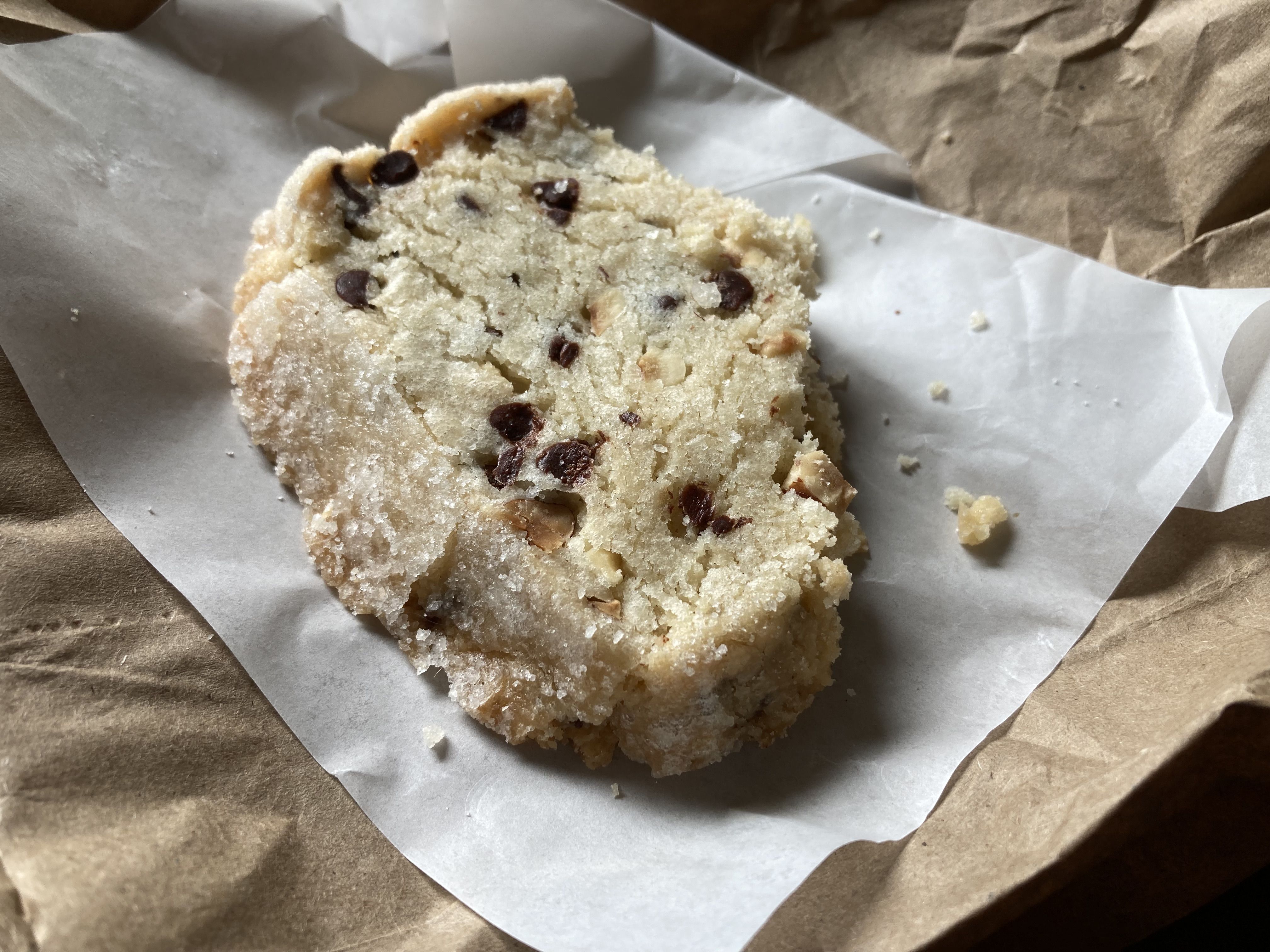 Part of a chocolate chip butter cookie, with crumbs, on a paper wrapper.