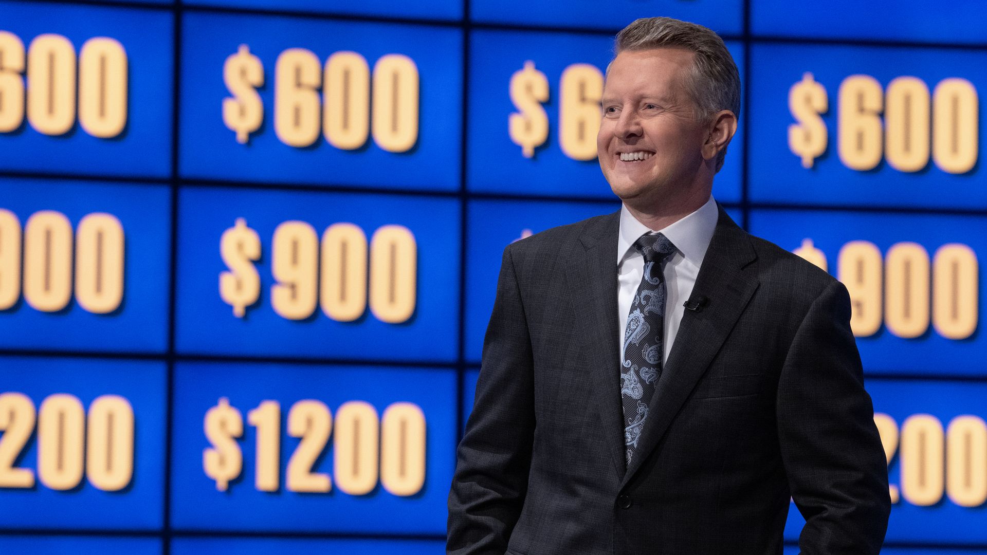 A person in a suit stands in front of a screen with multiple dollar figures