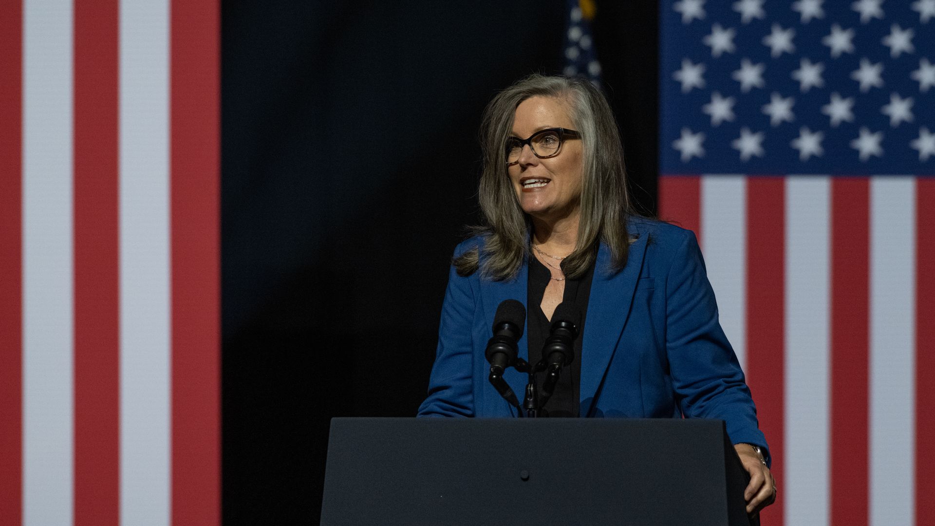 A woman standing at a podium and in front of the American flag.