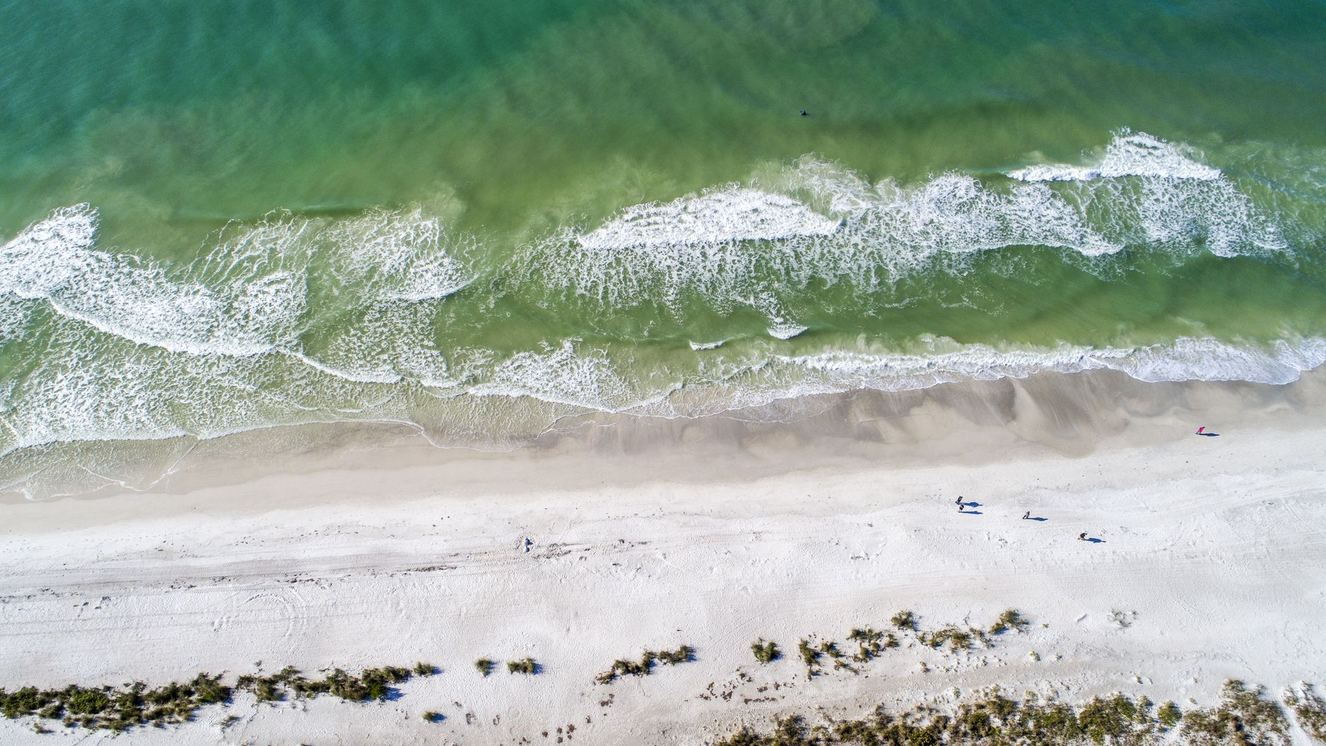 A photograph of waves crashing on a beige beach, near Anna Maria Island, Holmes Beach, Gulf of Mexico.