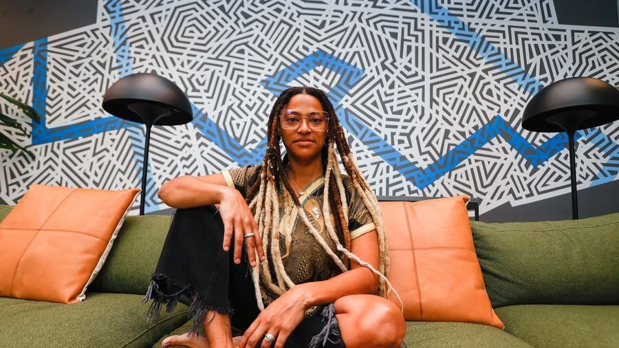 A woman with long braids sitting on a green couch with geometric art in the background.