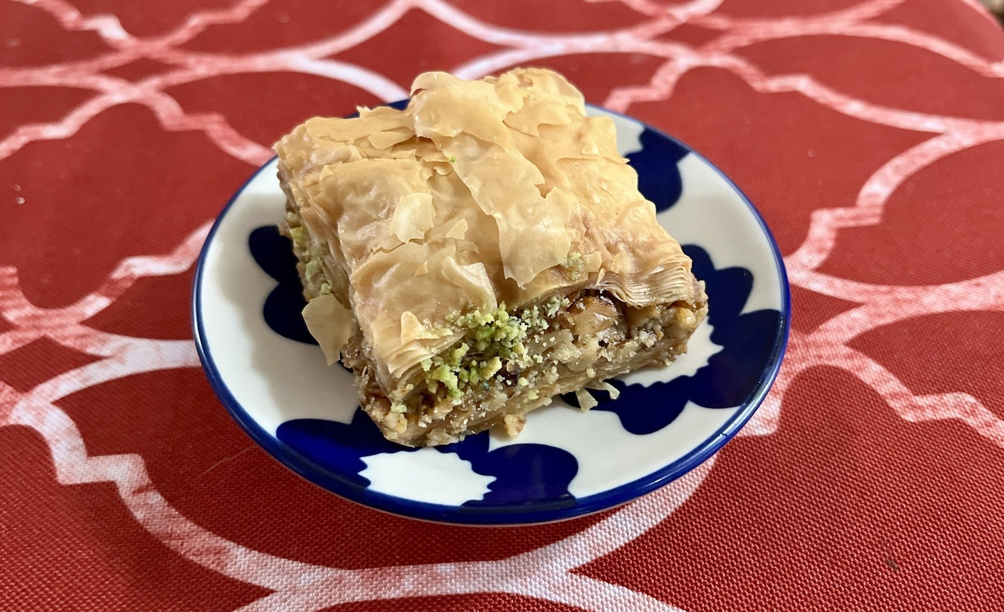 Square piece of baklava on blue and white plate on top of red tablecloth.