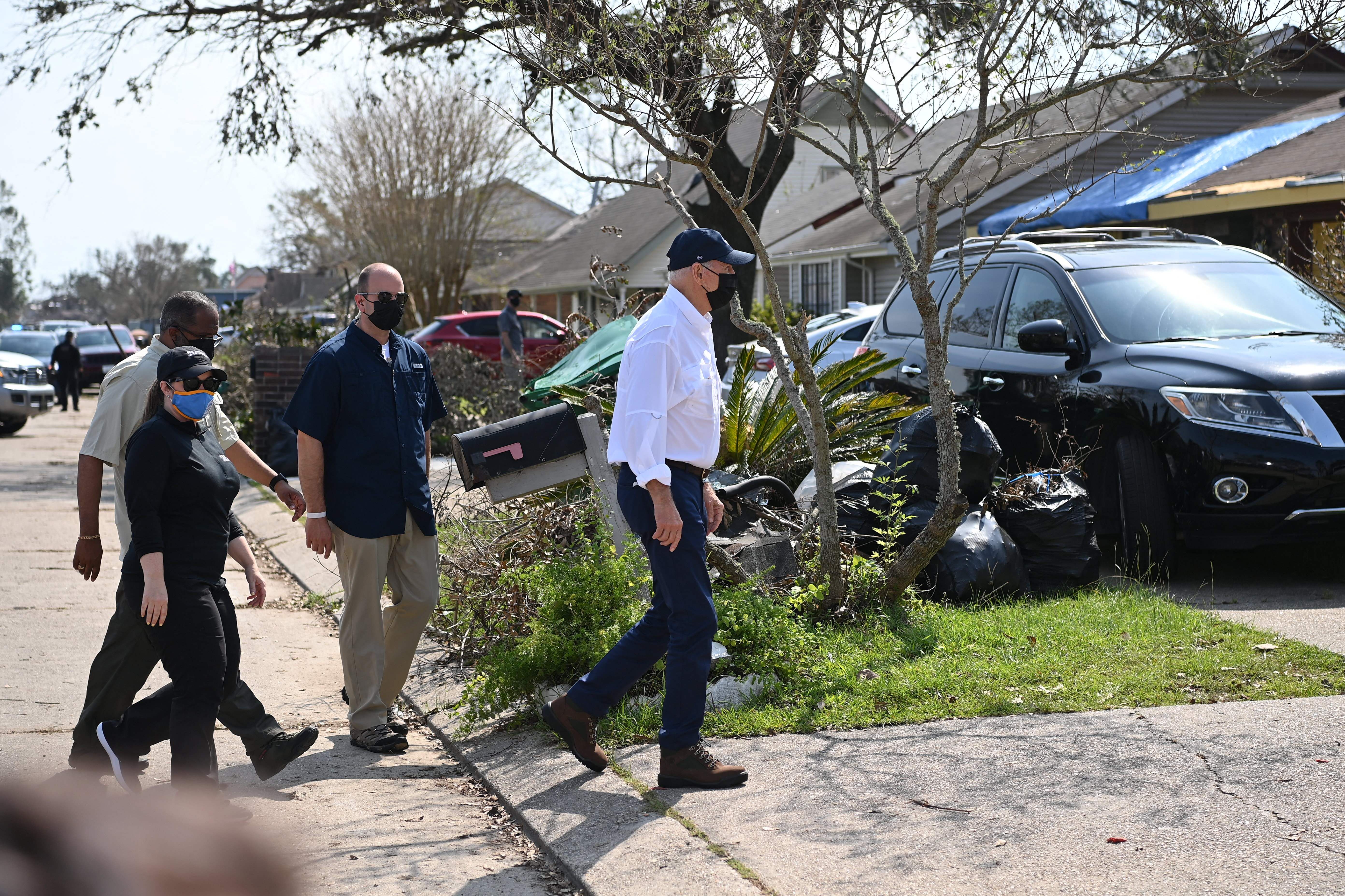 Photo of Joe Biden leading a line of people as they walk and survey damage in a residential neighborhood
