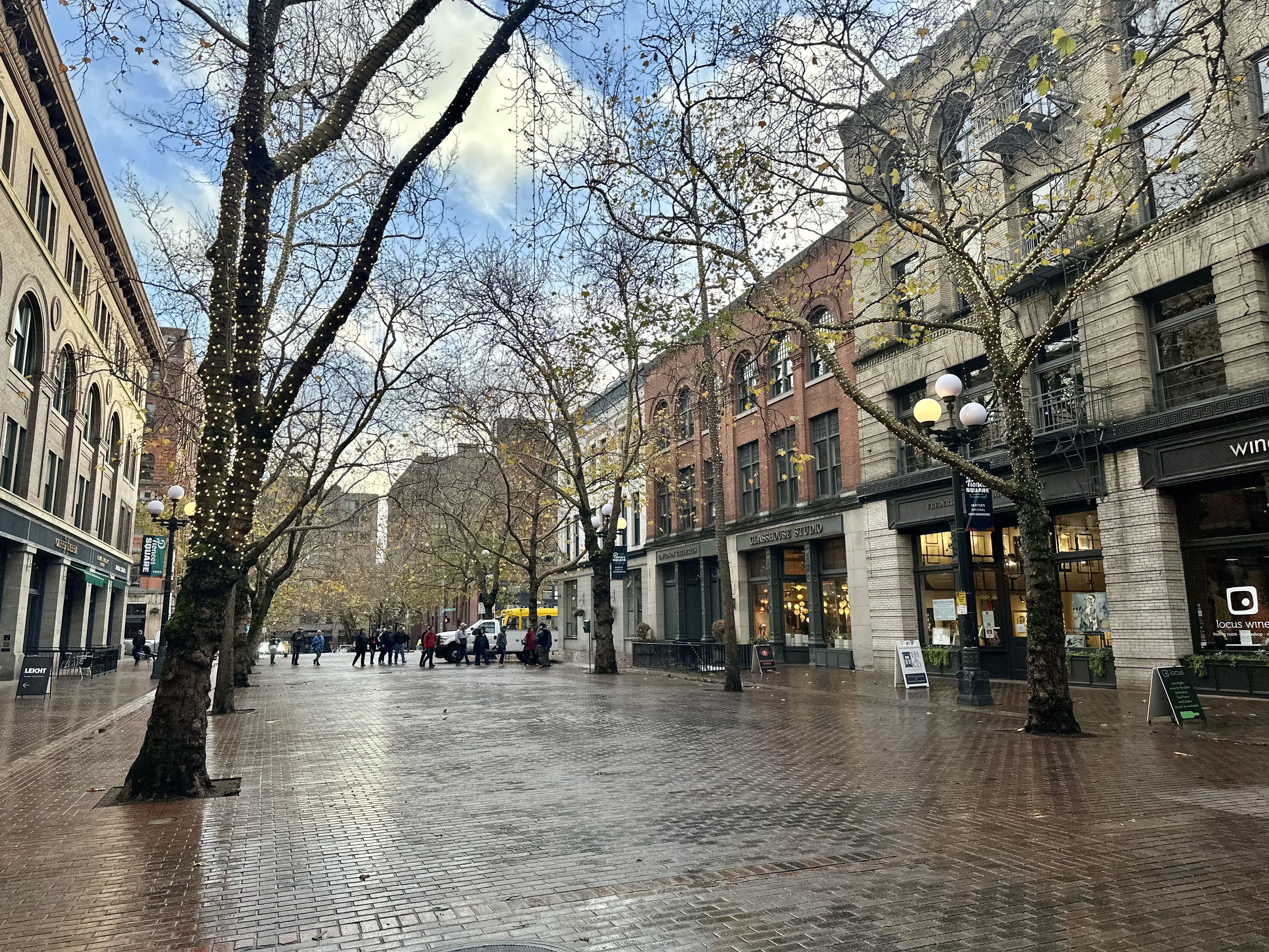 Brick buildings and a brick plaza lined by trees with lamp posts.