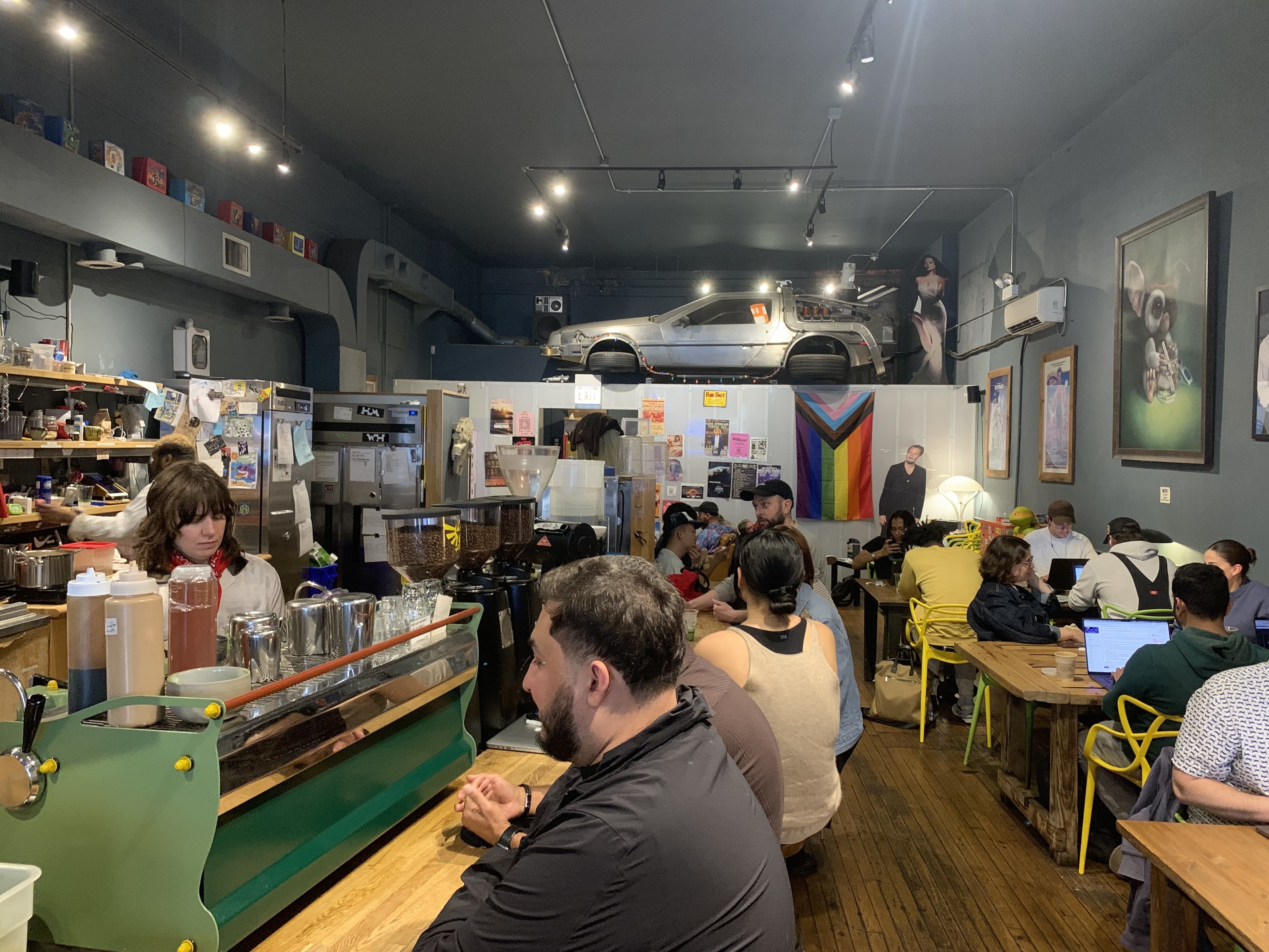 Photo of a coffee shop with several people at tables and chairs. 