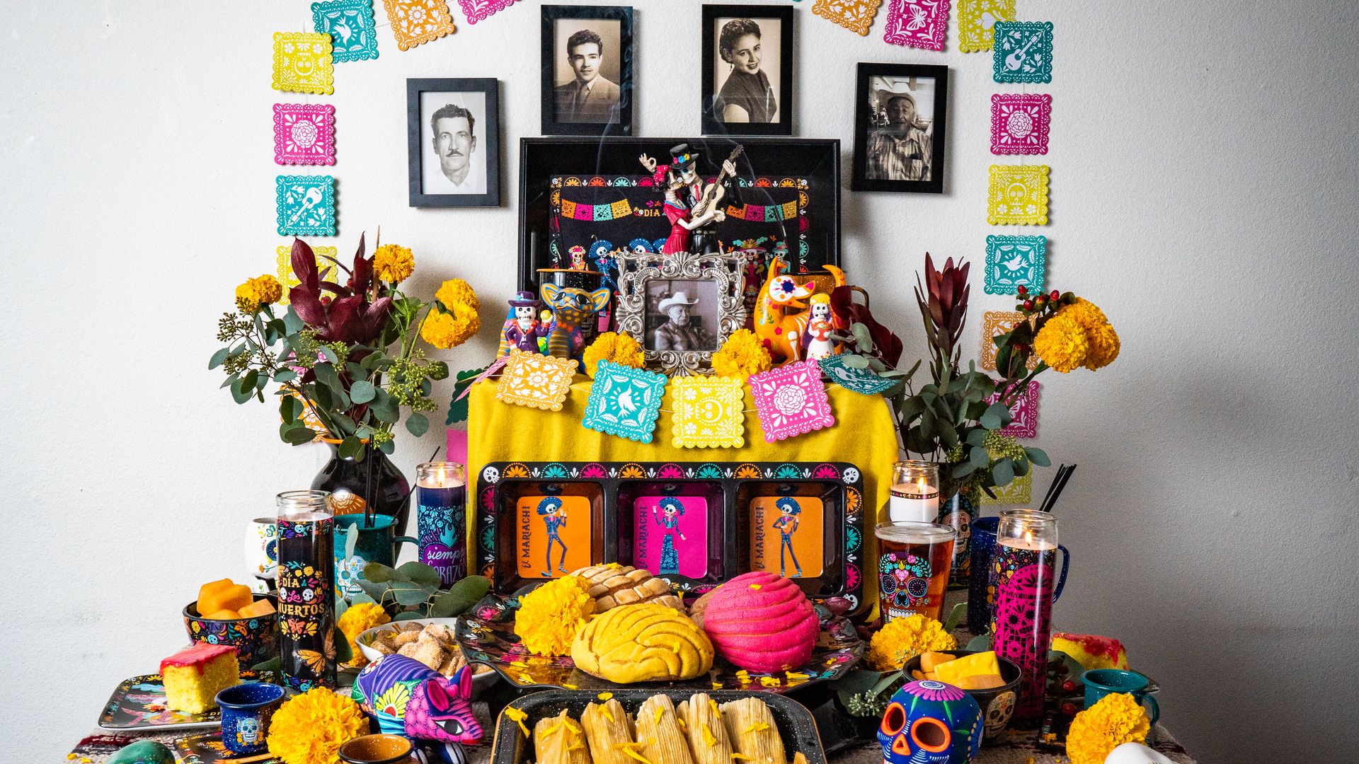 A table decorated as a brightly colored altar, with framed photos and papel picado. 