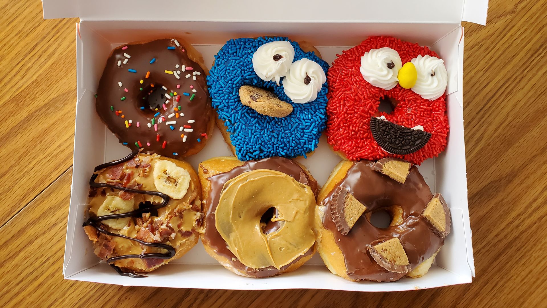 A box of six donuts, with two decorated as Elmo and Cookie Monster