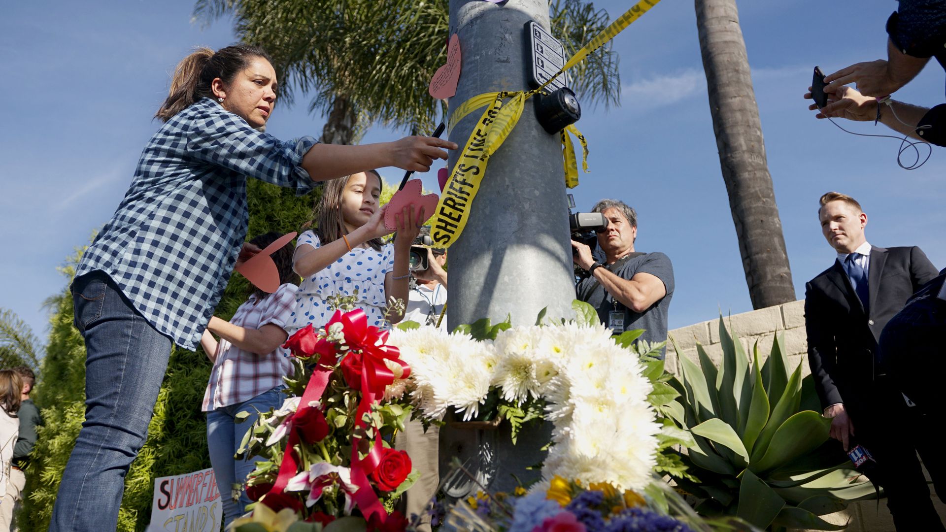 A woman and a young girl place notes on a light post near flowers across the street from the Chabad of Poway Synagogue after a shooting in Poway, California, Saturday.