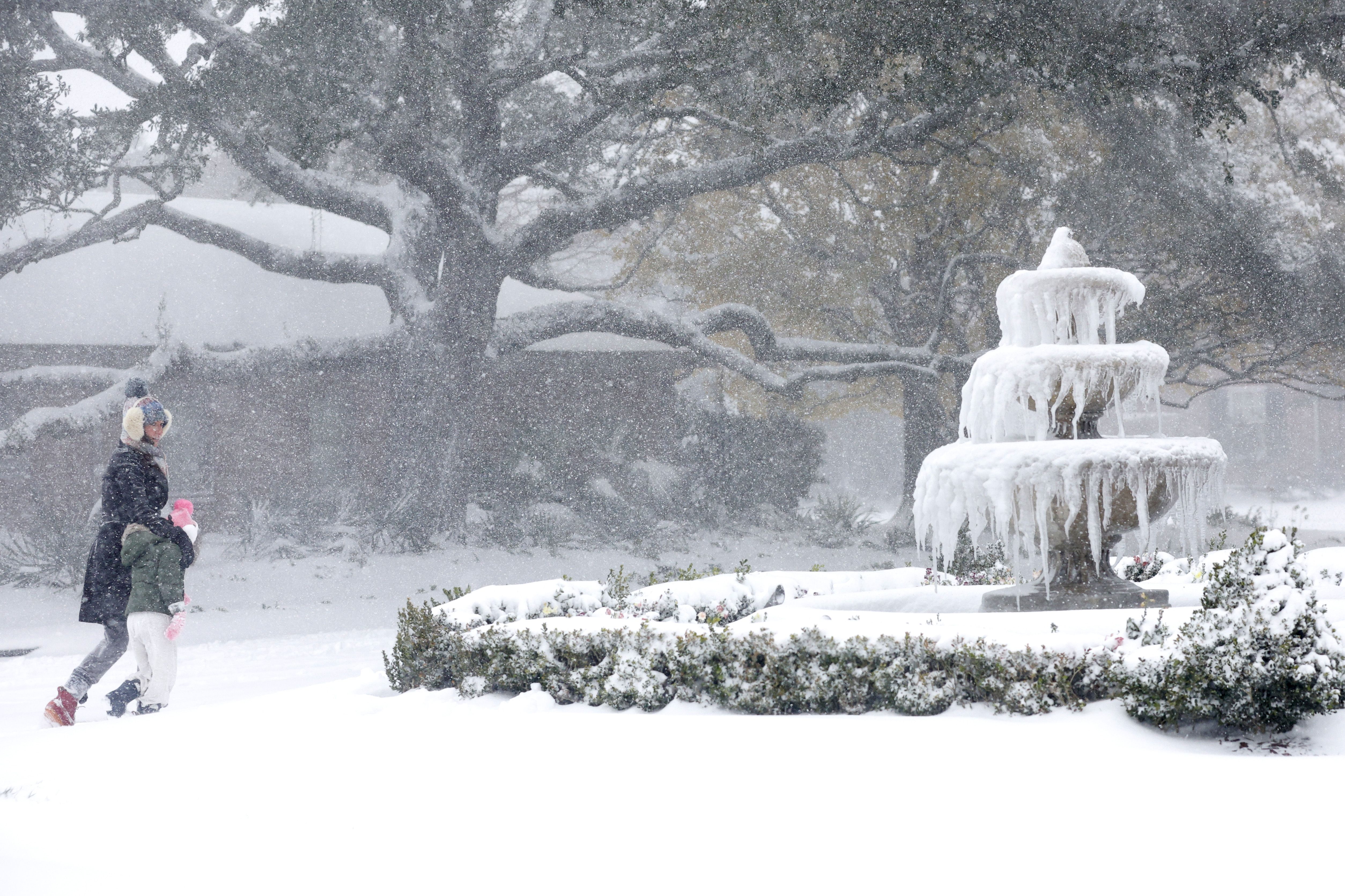 Photo shows people walking near a frozen fountain in the snow.