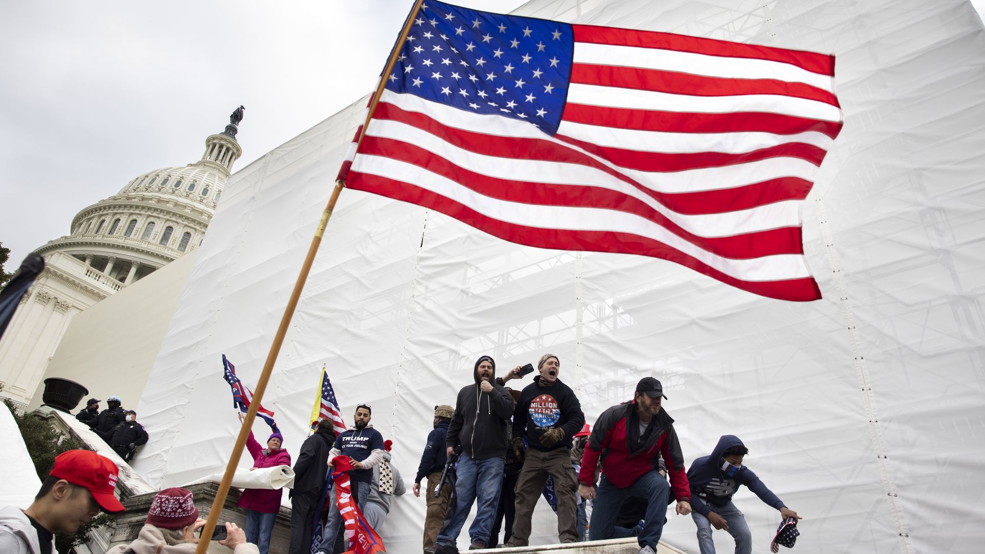 Photo of people yelling as an American flag is waved in the air