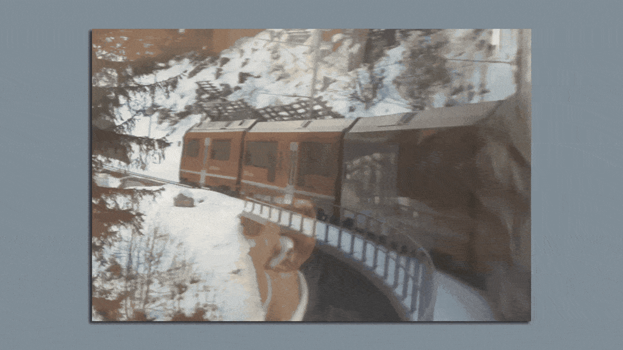 Orange train traveling on a curved snowy mountain track surrounded by trees and snow-covered landscape under a blue sky.