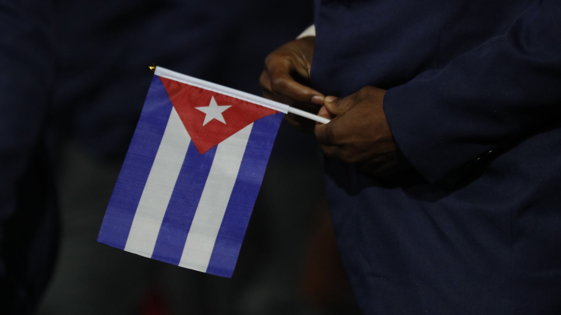 In this image, a man holds a small Cuban flag