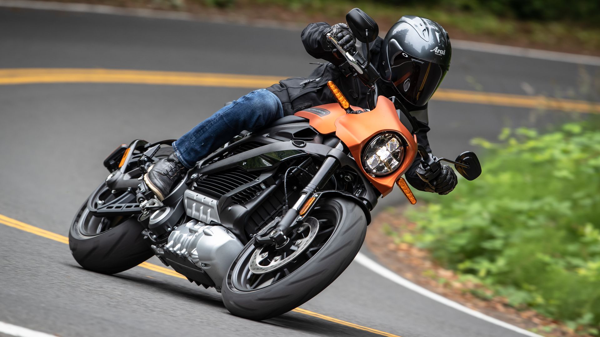 A helmet-wearing motorcyclist leans around a corner on an orange bike